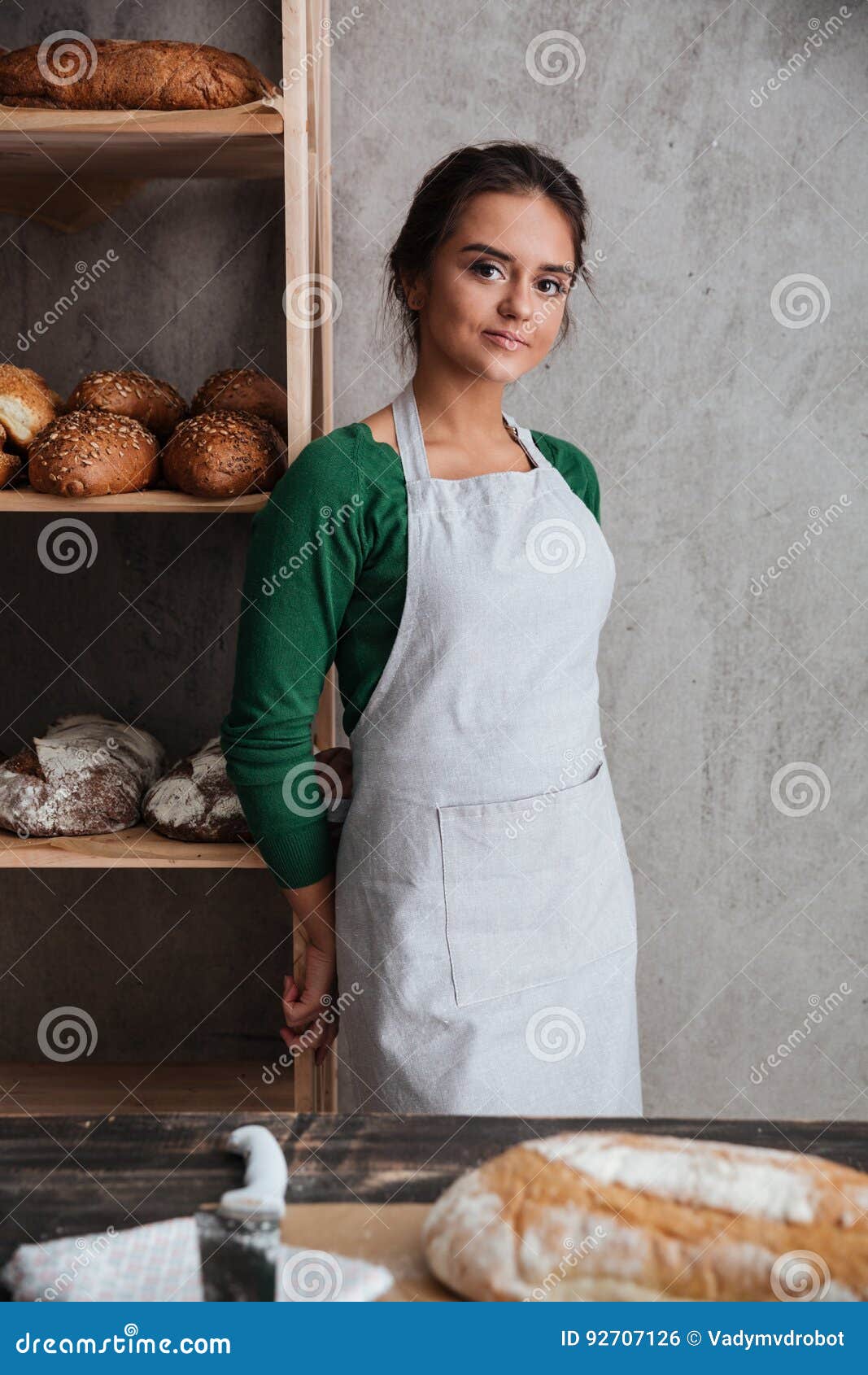 Happy Young Lady Baker Standing at Bakery Near Bread. Stock Photo