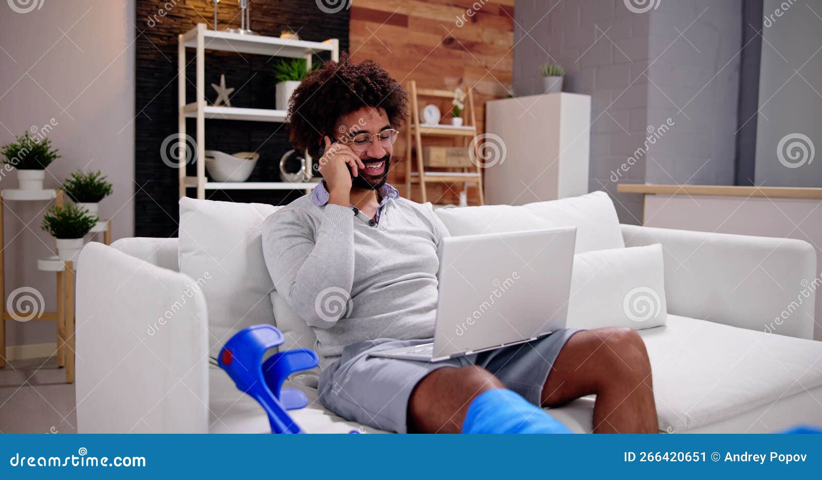 happy young man with broken leg sitting on sofa talking