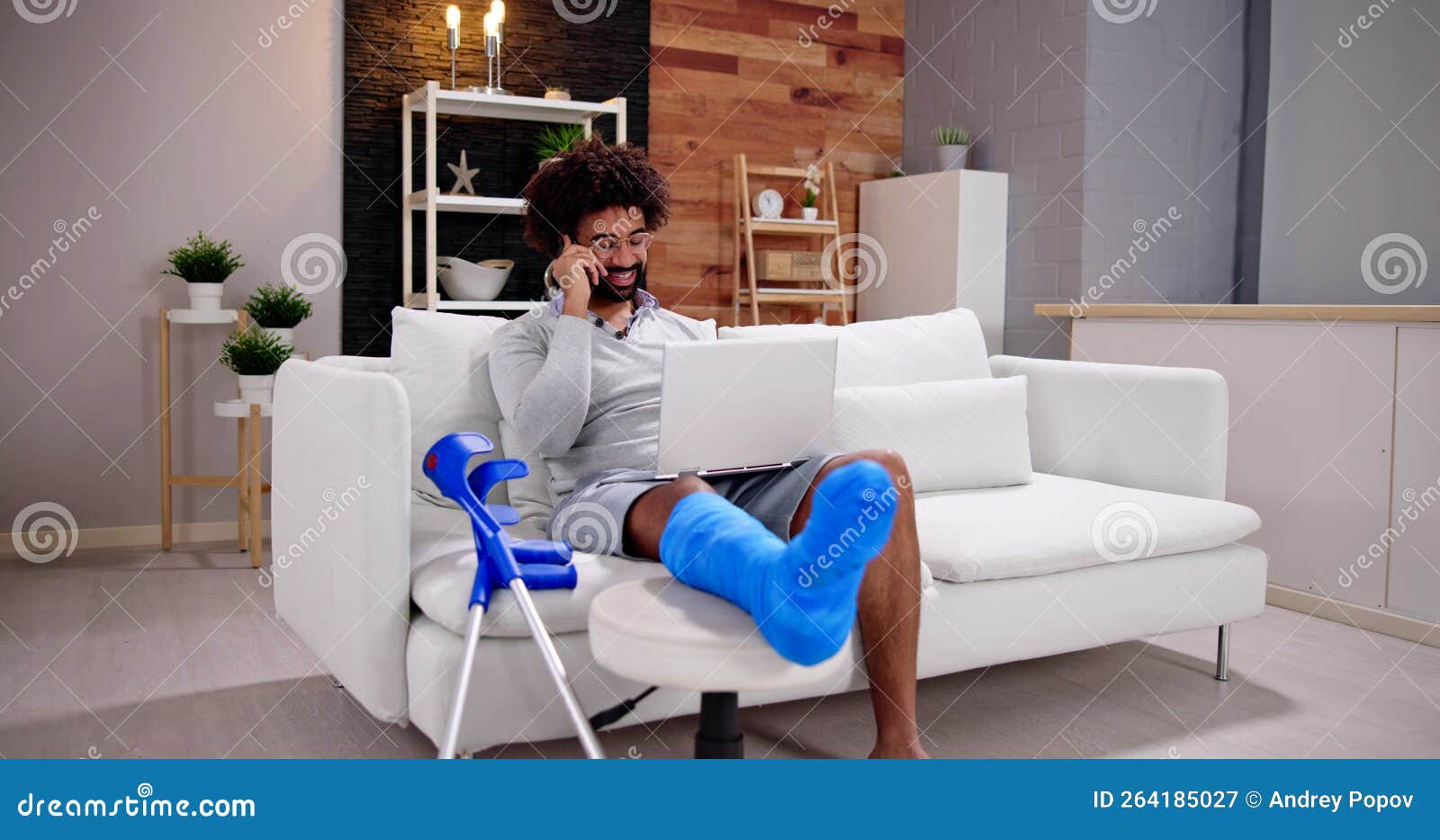 happy young man with broken leg sitting on sofa talking