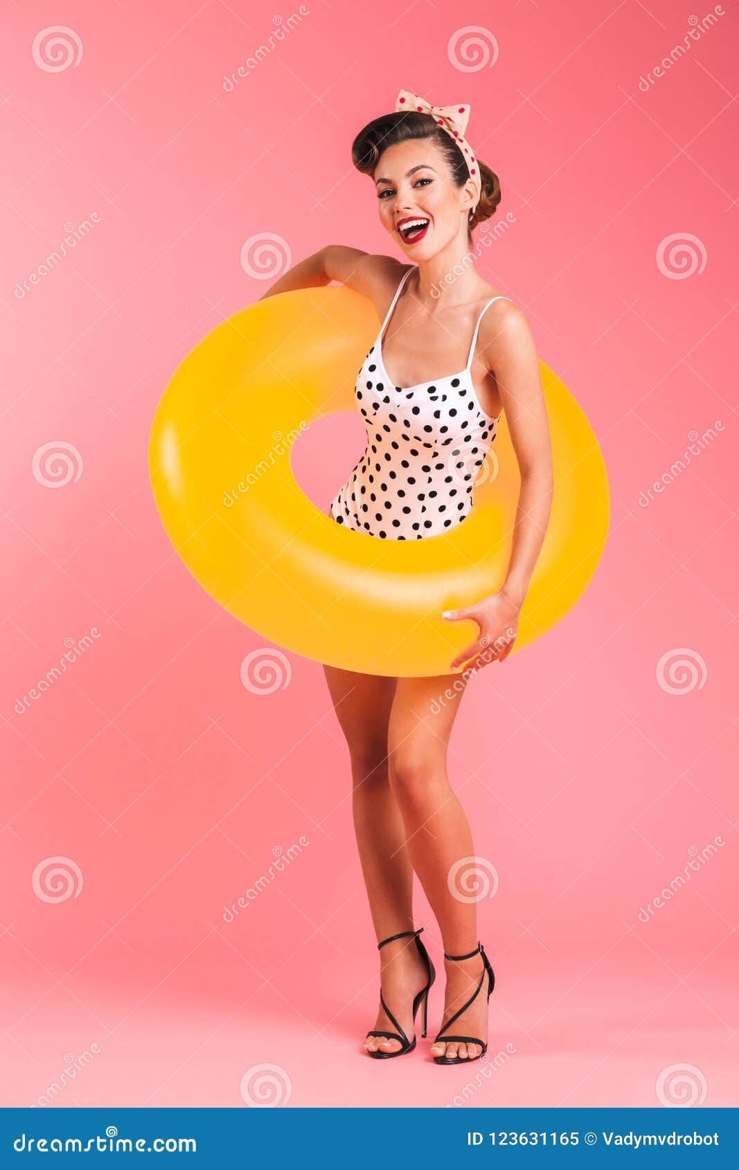 Happy young pin-up woman in swimwear with inflatable ring. Photo of happy young pin-up woman over pink background wall in swimwear with inflatable ring.