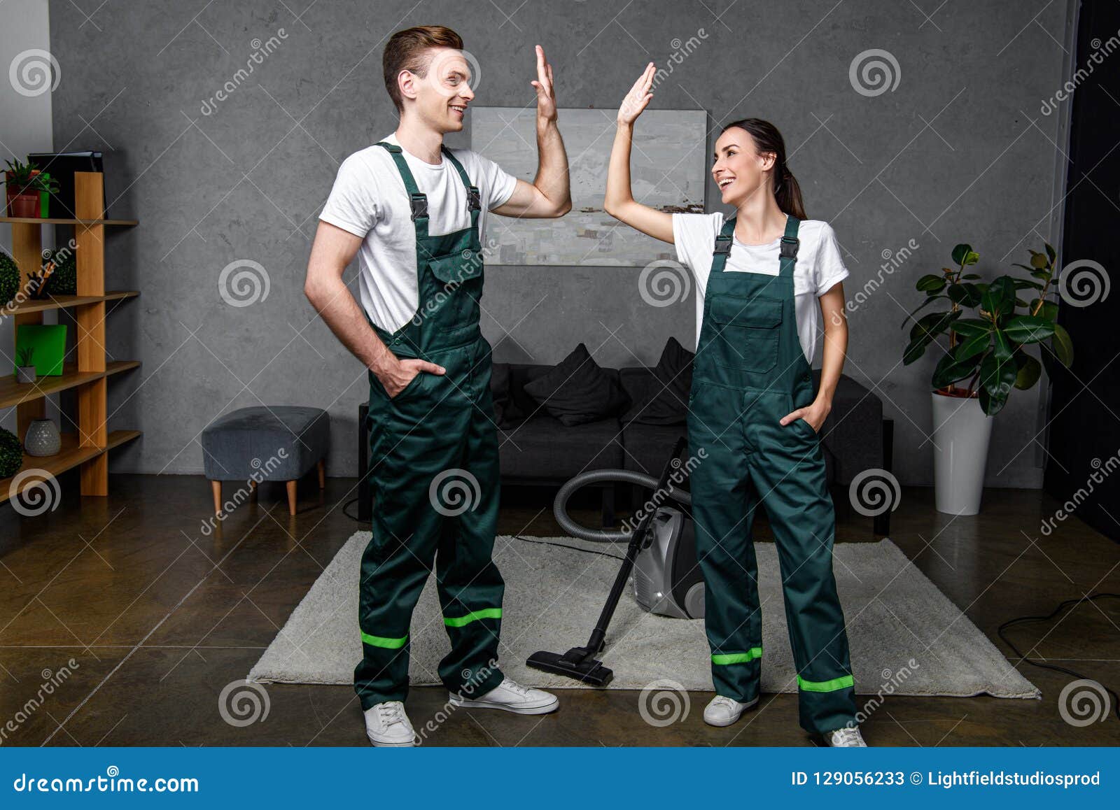 happy young professional cleaners smiling each other and giving high
