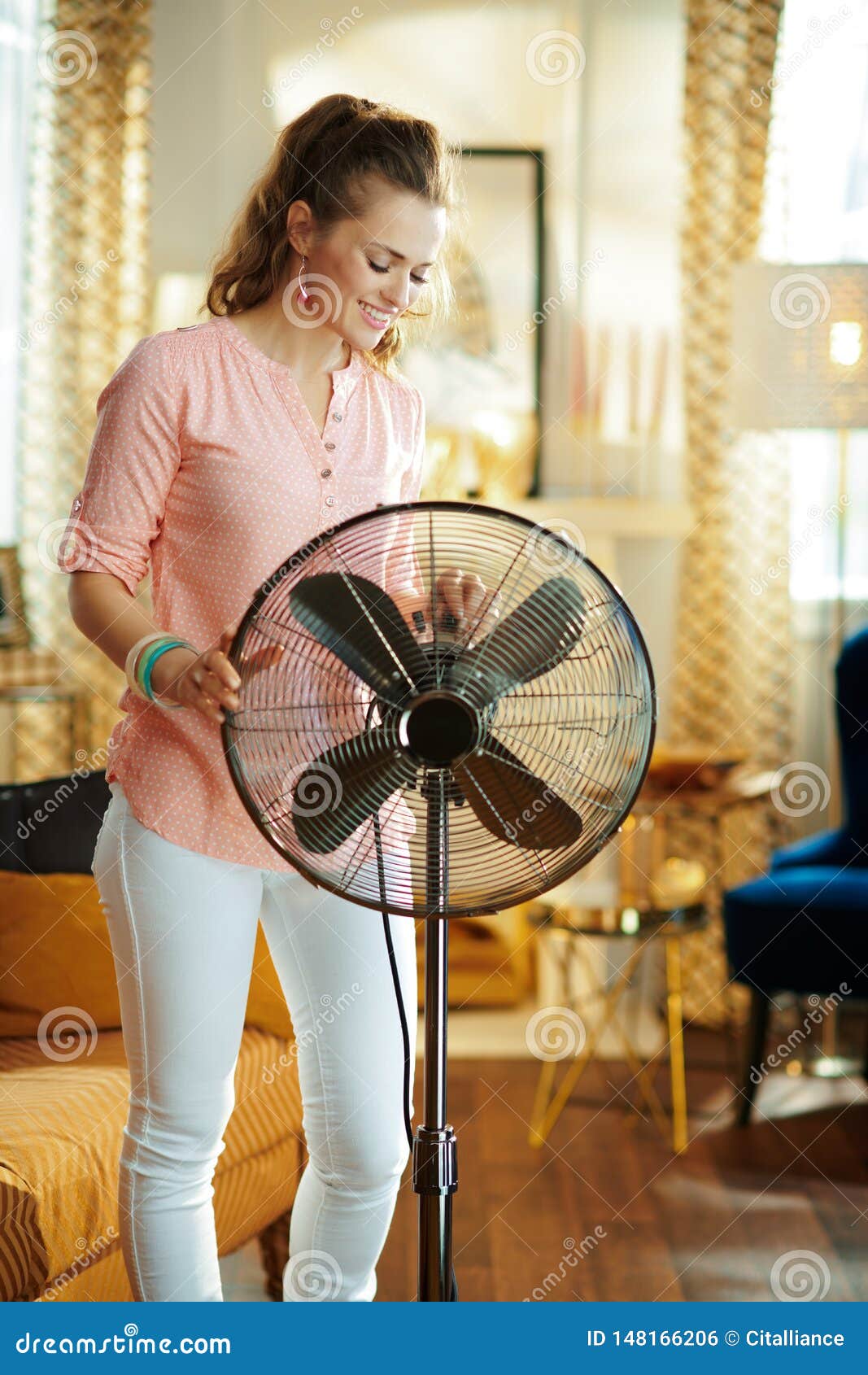 happy young woman swtitching on metallic floor standing fan