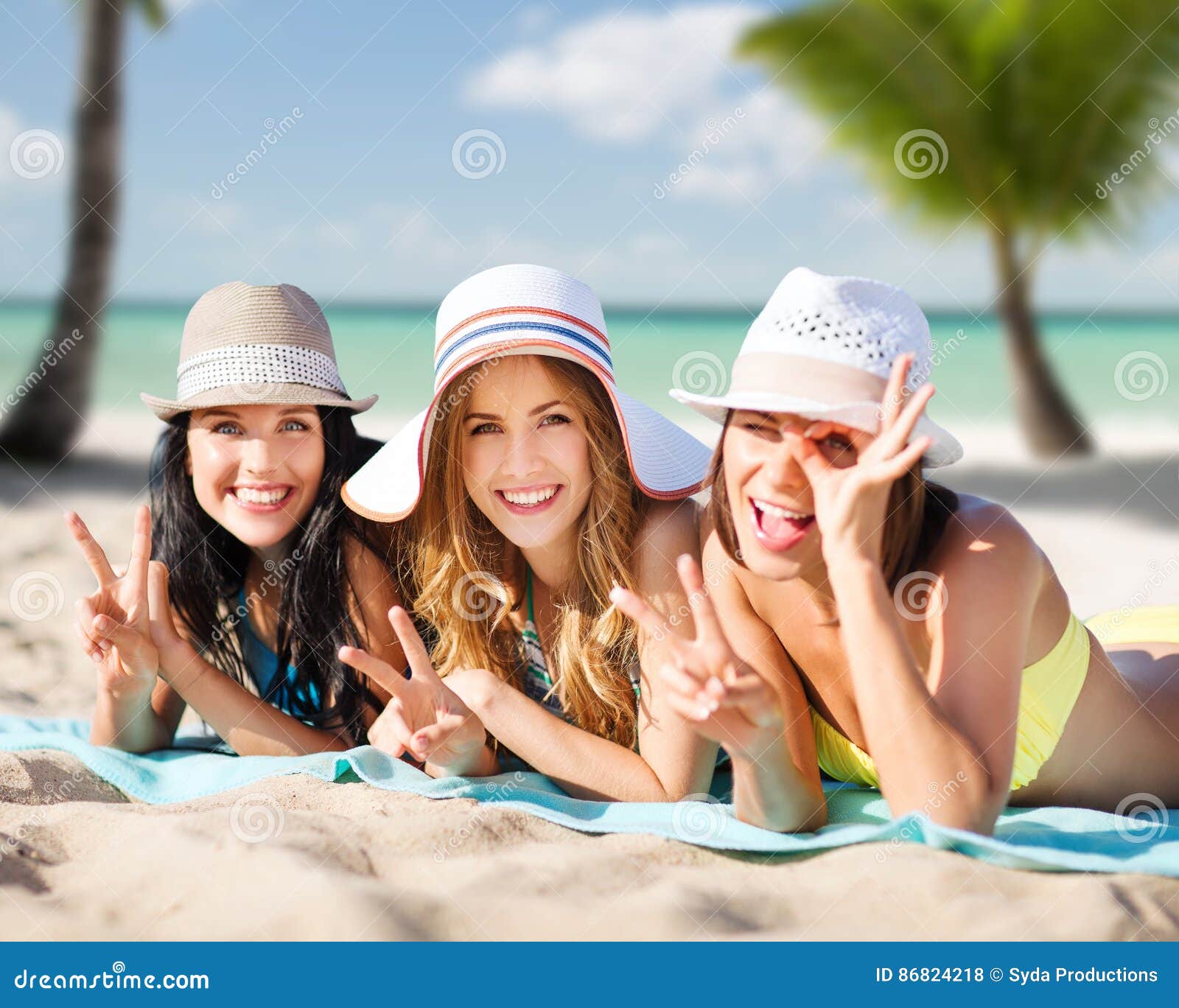 Happy young women in bikinis on summer beach. Summer holidays, travel, people and vacation concept - happy young women in bikinis sunbathing over exotic tropical beach with palm trees and sea shore background