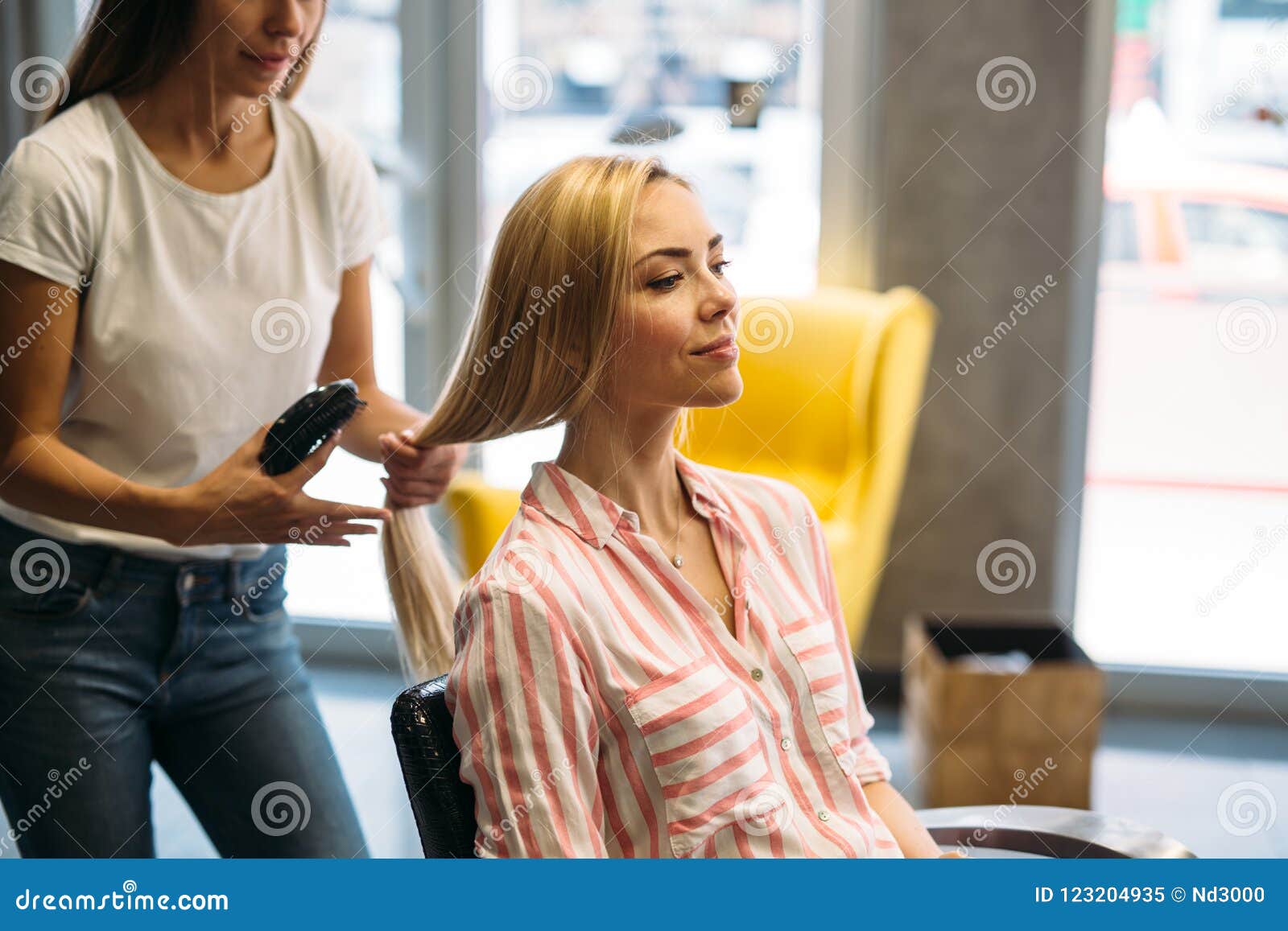Happy Young Woman And Hairdresser With Fan Making Hot Styling