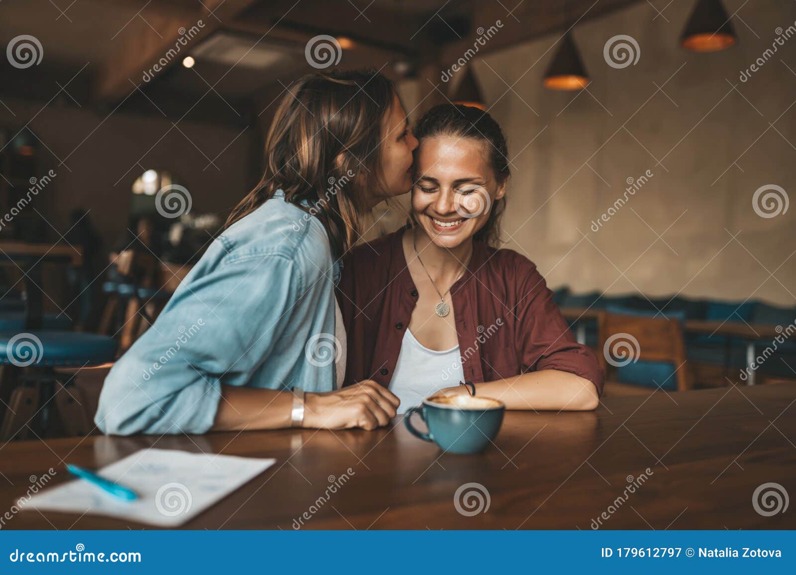 Happy Young Woman Kissing Her Girlfriend Sitting In A Cafe Stock Imag