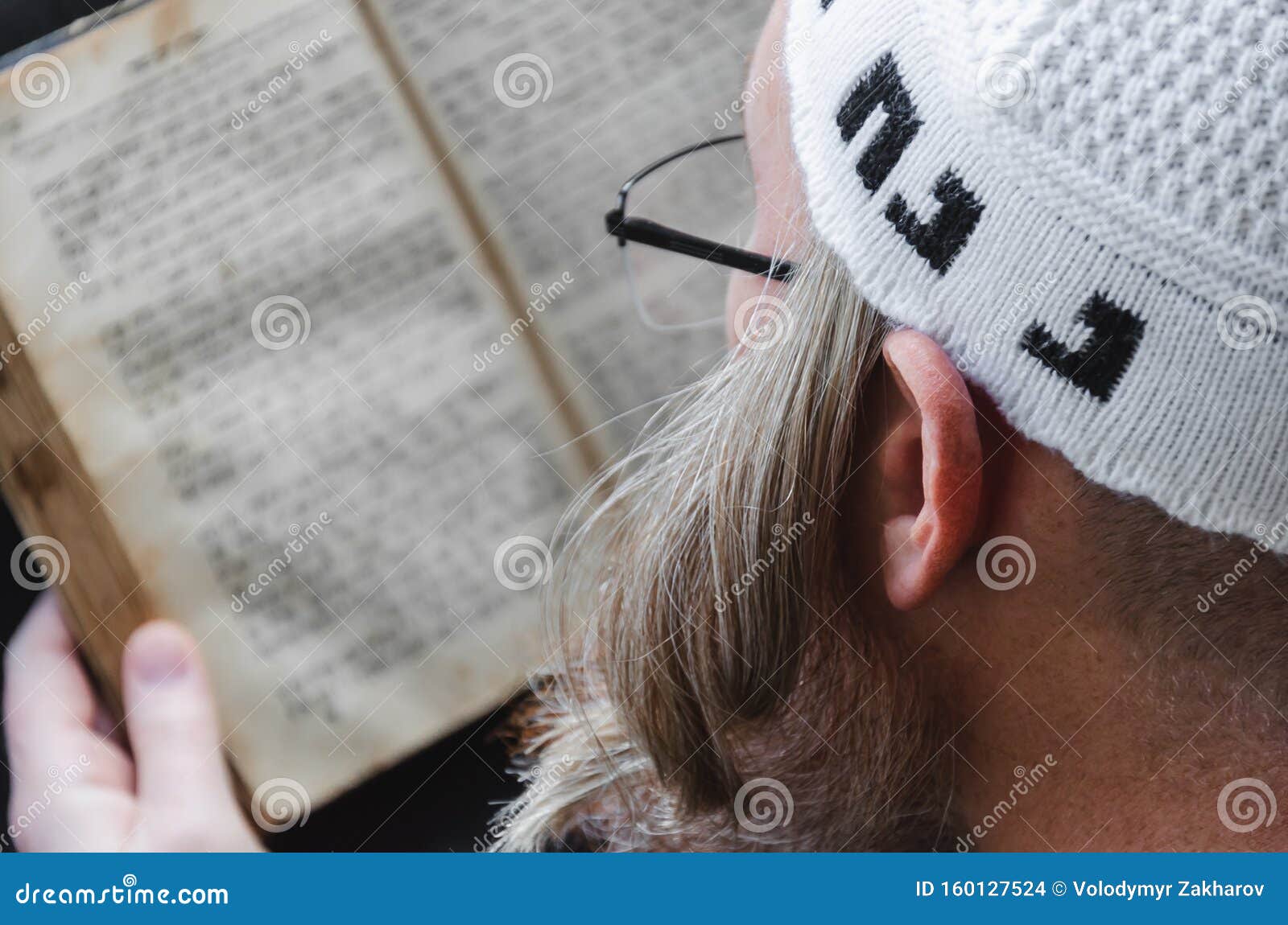 A Hasidic reads Siddur. Religious orthodox with a red beard and with pace in a white bale praying. Closeup. A Hasidic reads Siddur. Religious orthodox with a red beard and with pace in a white bale praying. On the bale is an inscription Rabbi Nahman from Uman. Close-up.