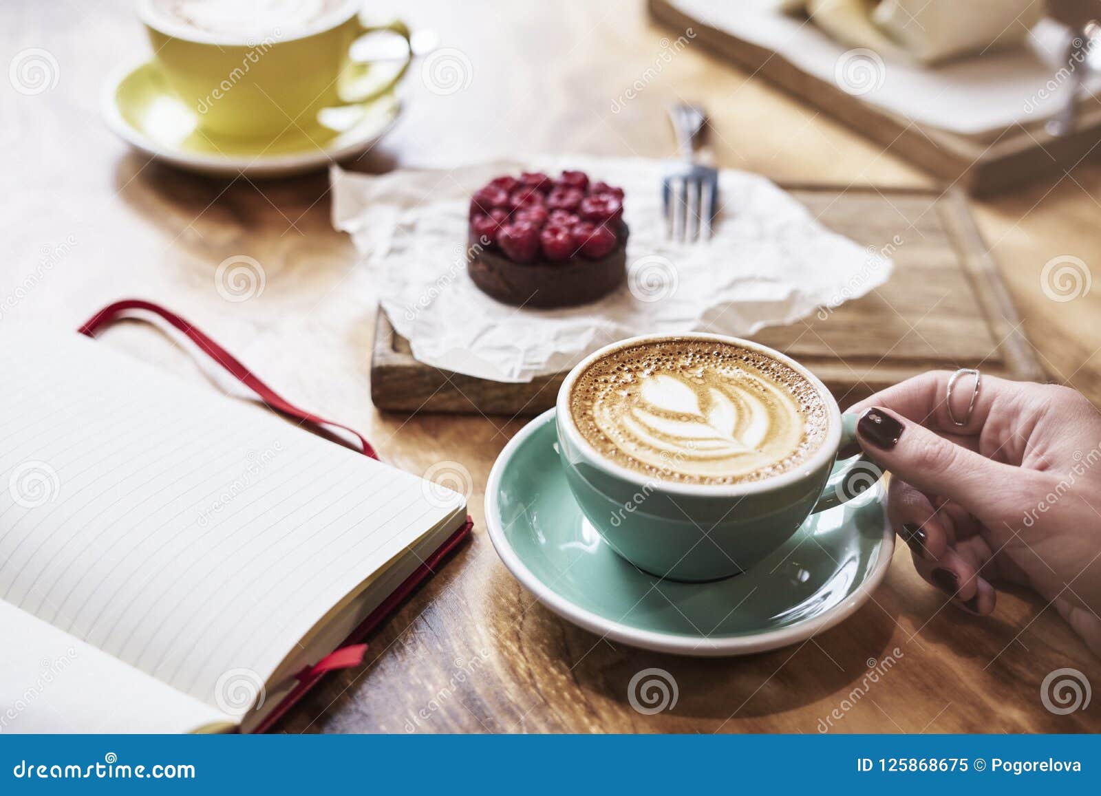 having lunch with coffee flat white and sweet chocolate cookie in a cafe or restaurant. woman hand holds a green cup.