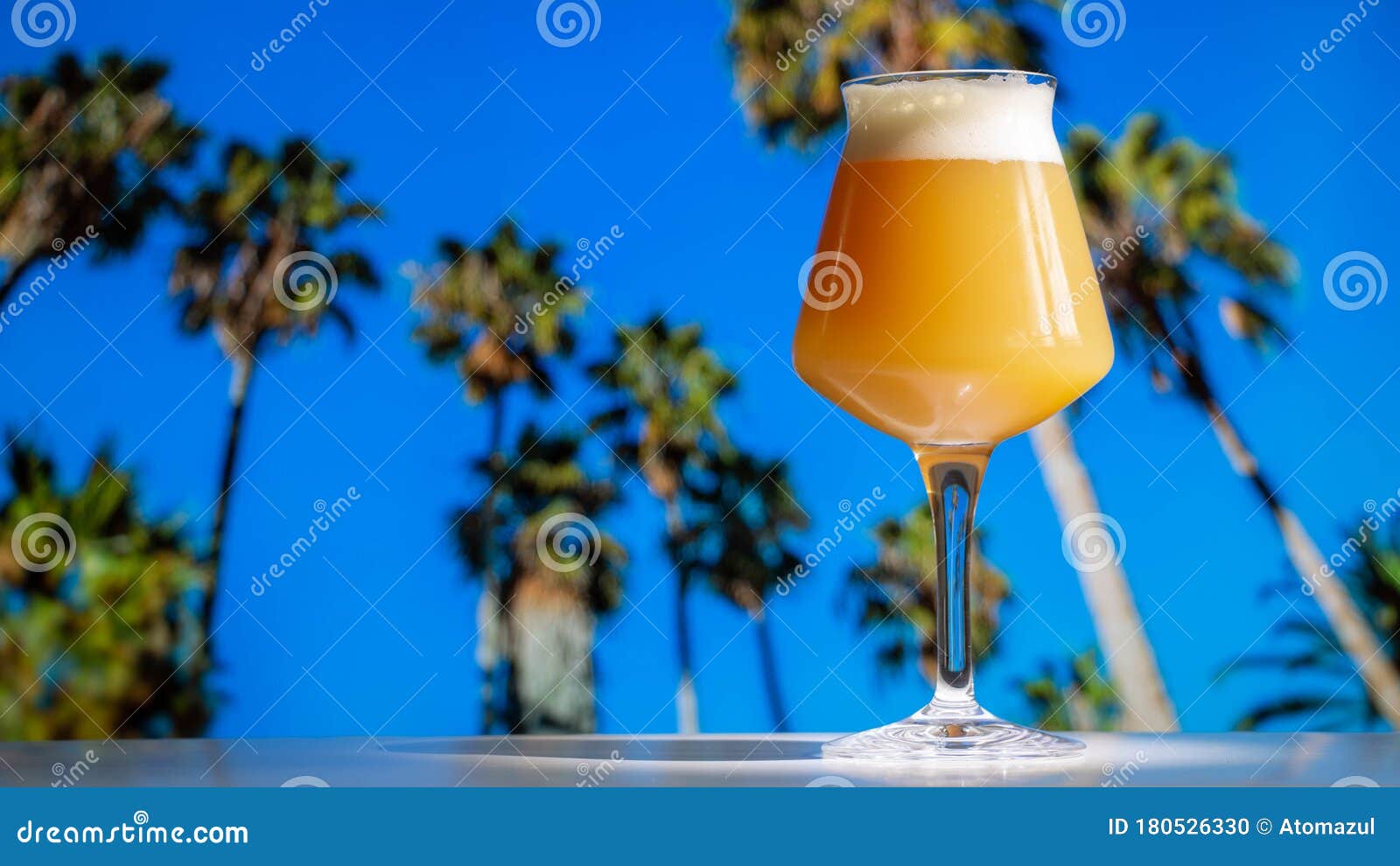 hazy ipa craft beer in teku glass with tropical palm trees and blue sky