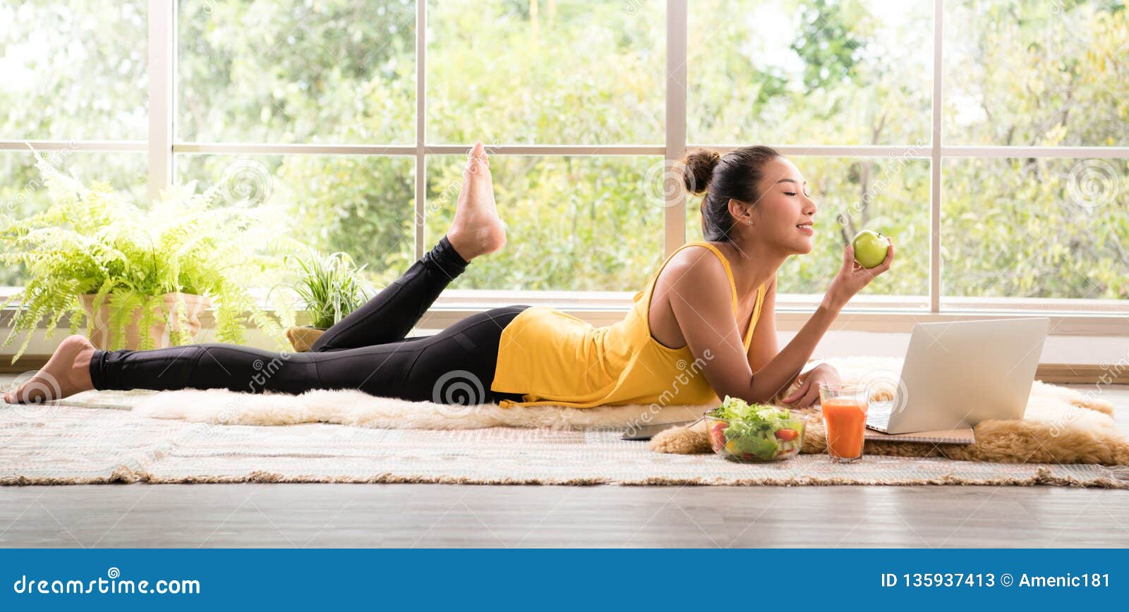 healthy asian woman lying on the floor eating salad looking relaxed and comfortable