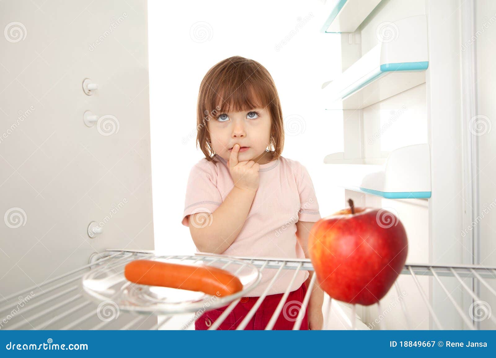 Healthy eating choice. Cute young girl looking in open refrigerator deciding between healthy apple and unhealthy hot dog.