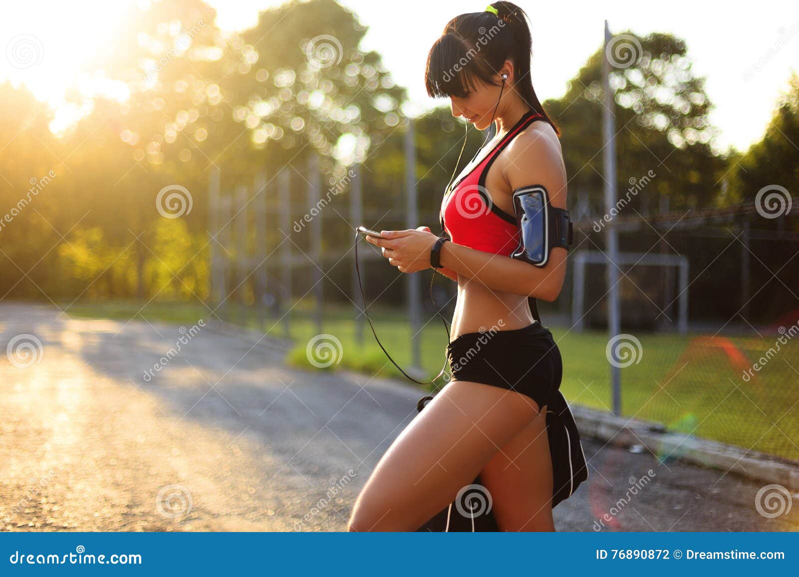 Fitness. Woman Doing Workout Exercise On Street. Beautiful Fit Girl Wearing  Fitness Tracker, Headphones And Armband Phone Case Stretching Her Long Legs  Outdoors. Sports Devices. High Resolution Stock Photo, Picture and Royalty