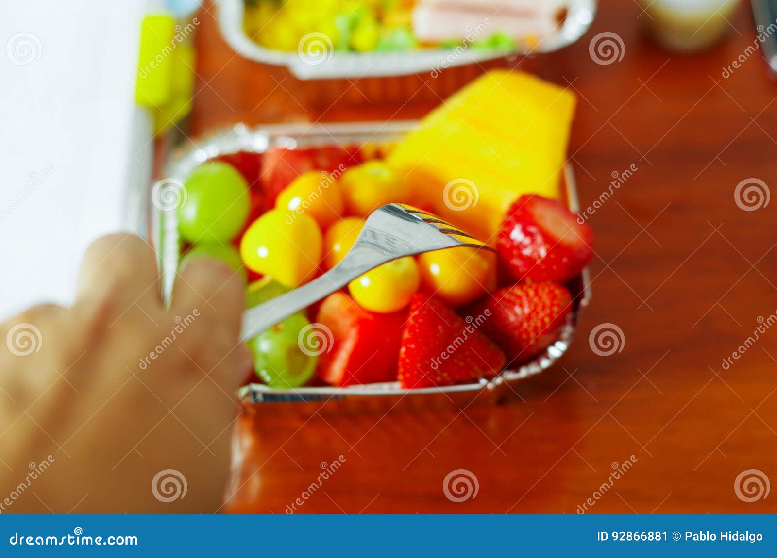healthy man using a fork to eat in the office a delicious fresh fruit salad on aluminium box on wooden table above view