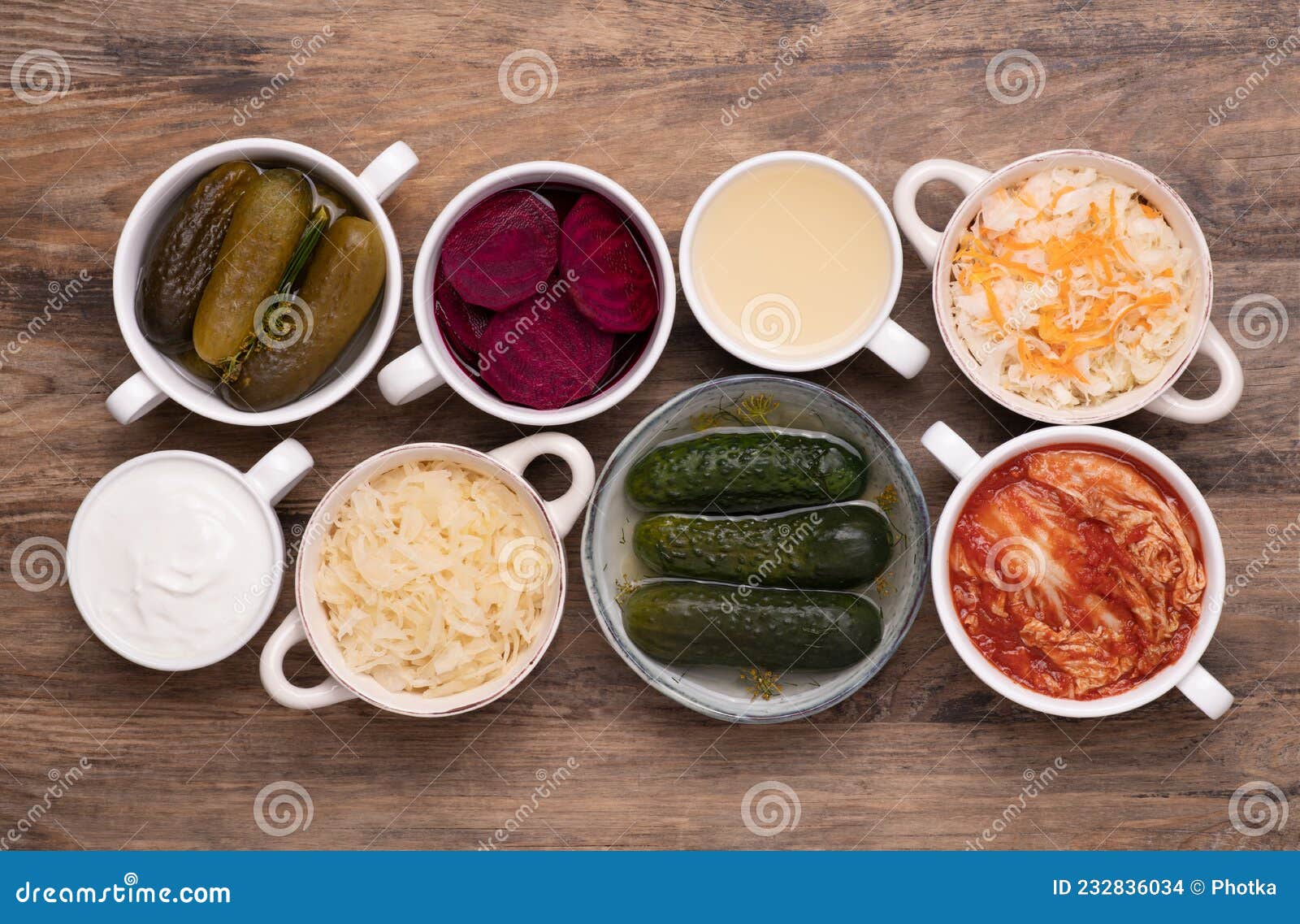 healthy probiotic fermented foods in cups and bowls on wooden table, top view