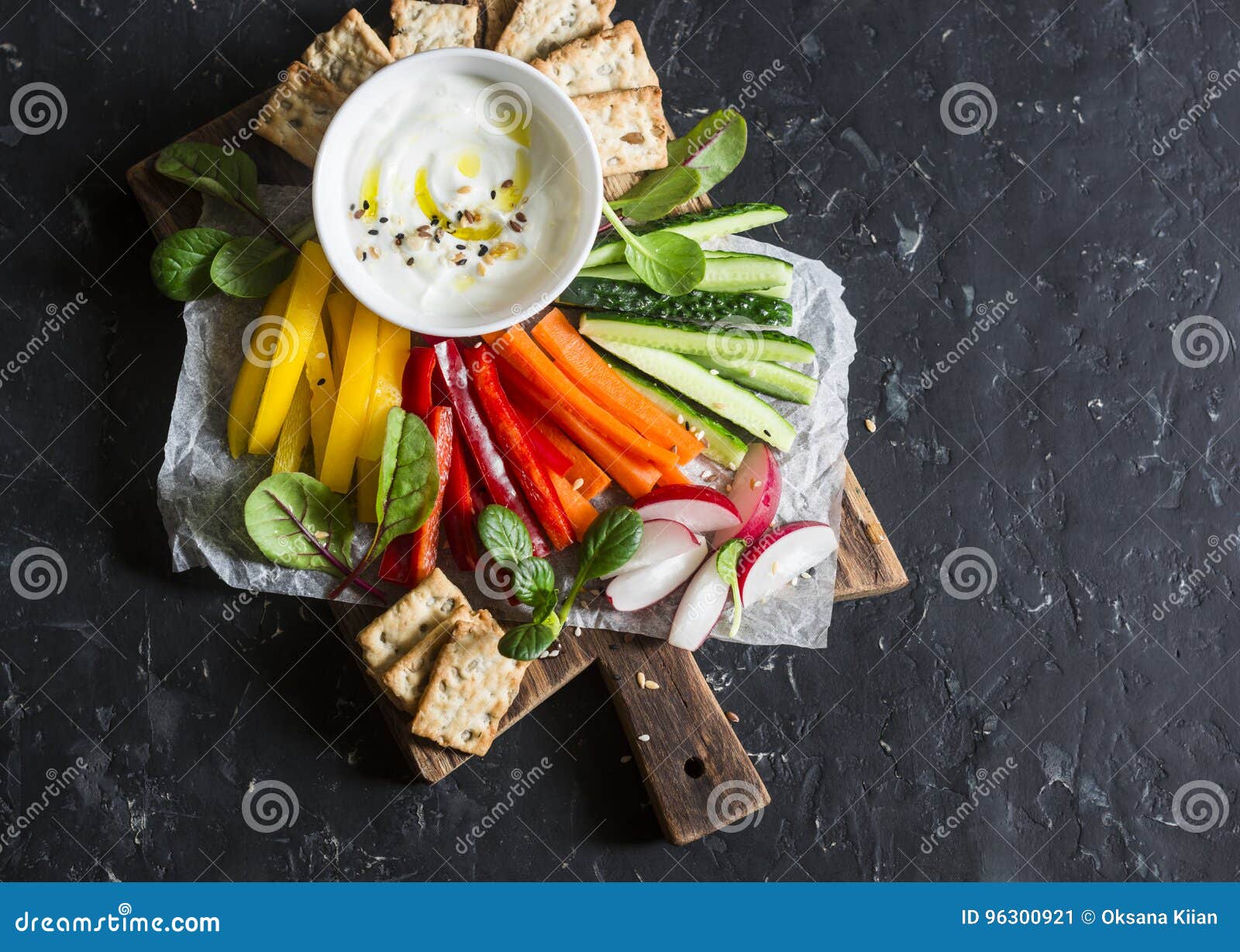healthy snack - raw vegetables and yogurt sauce on a wooden cutting board, on a dark background, top view. vegetarian healthy food