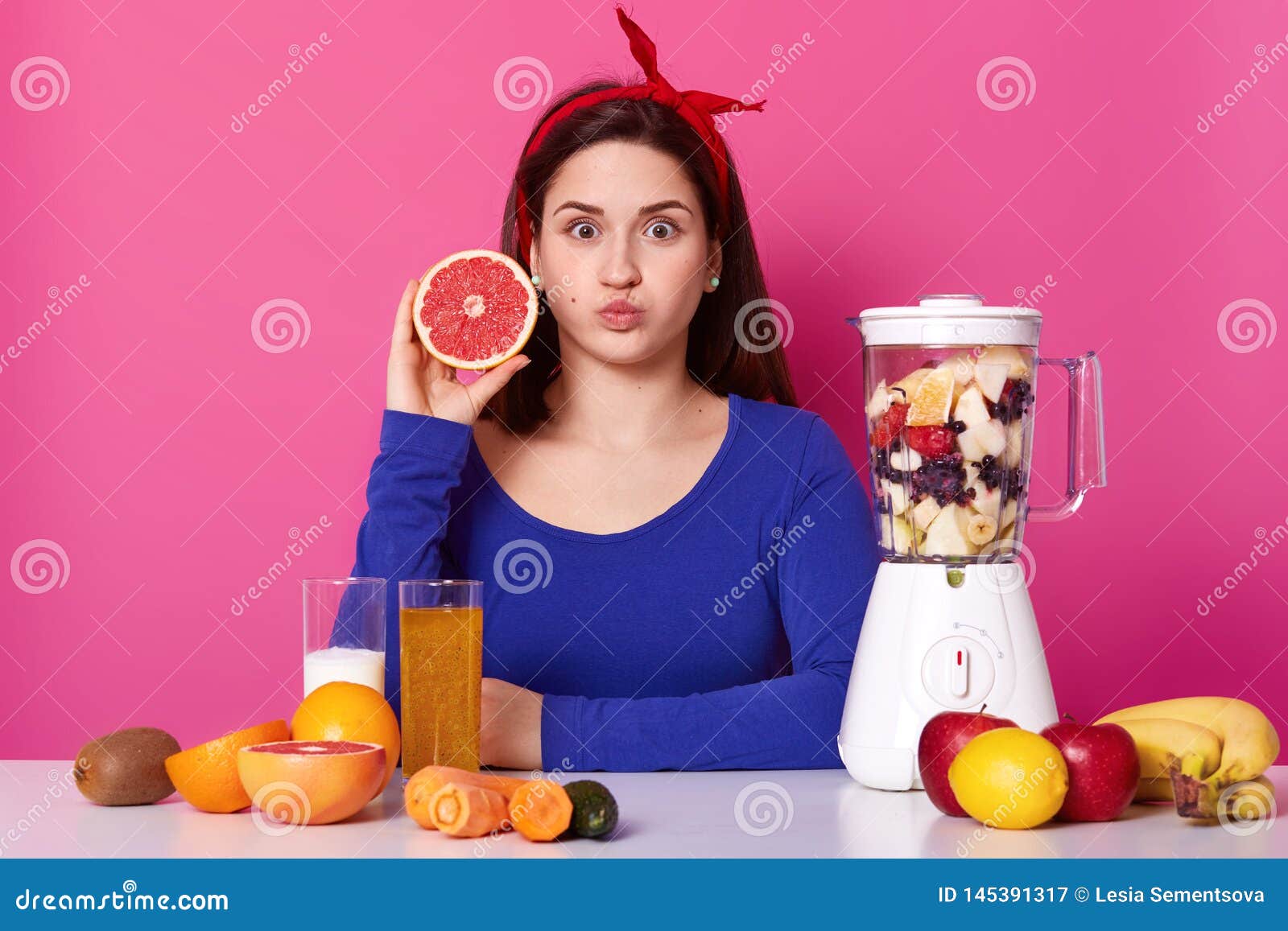 healthy vegeterian girl openes her eyes widely, blows her mouth, looking directly at camera, holding fruit in one hand. different