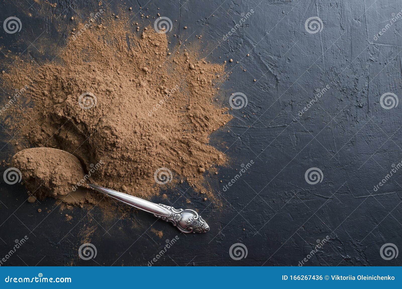 heap of cocoa powder and spoon full of it on the black kitchen yable.empty space for text