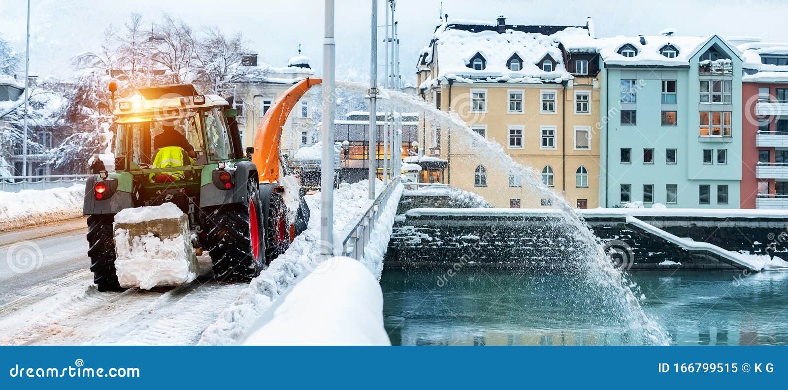 Heavy municipal services machinery removing snow from city streets. Big tractor snowblower blowing snow from bridge road into river. Cleaning streets and snow removal after snowfall at winter season.