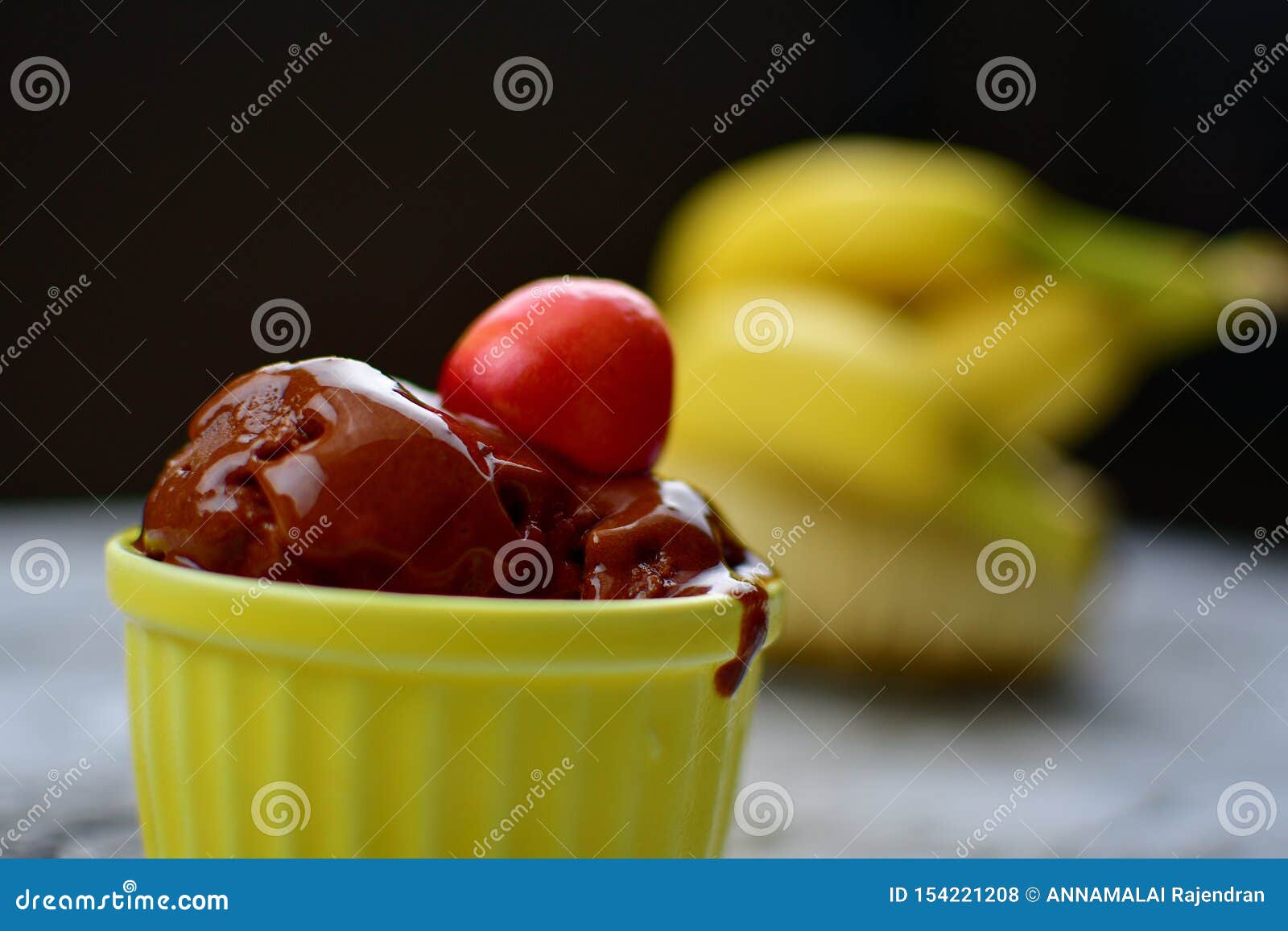 Helado de Chocloate con el backgroud de Cherry Topping y del plátano. Helado de Chocloate con Cherry Topping y el plátano borroso en el tablero de la mesa de mármol