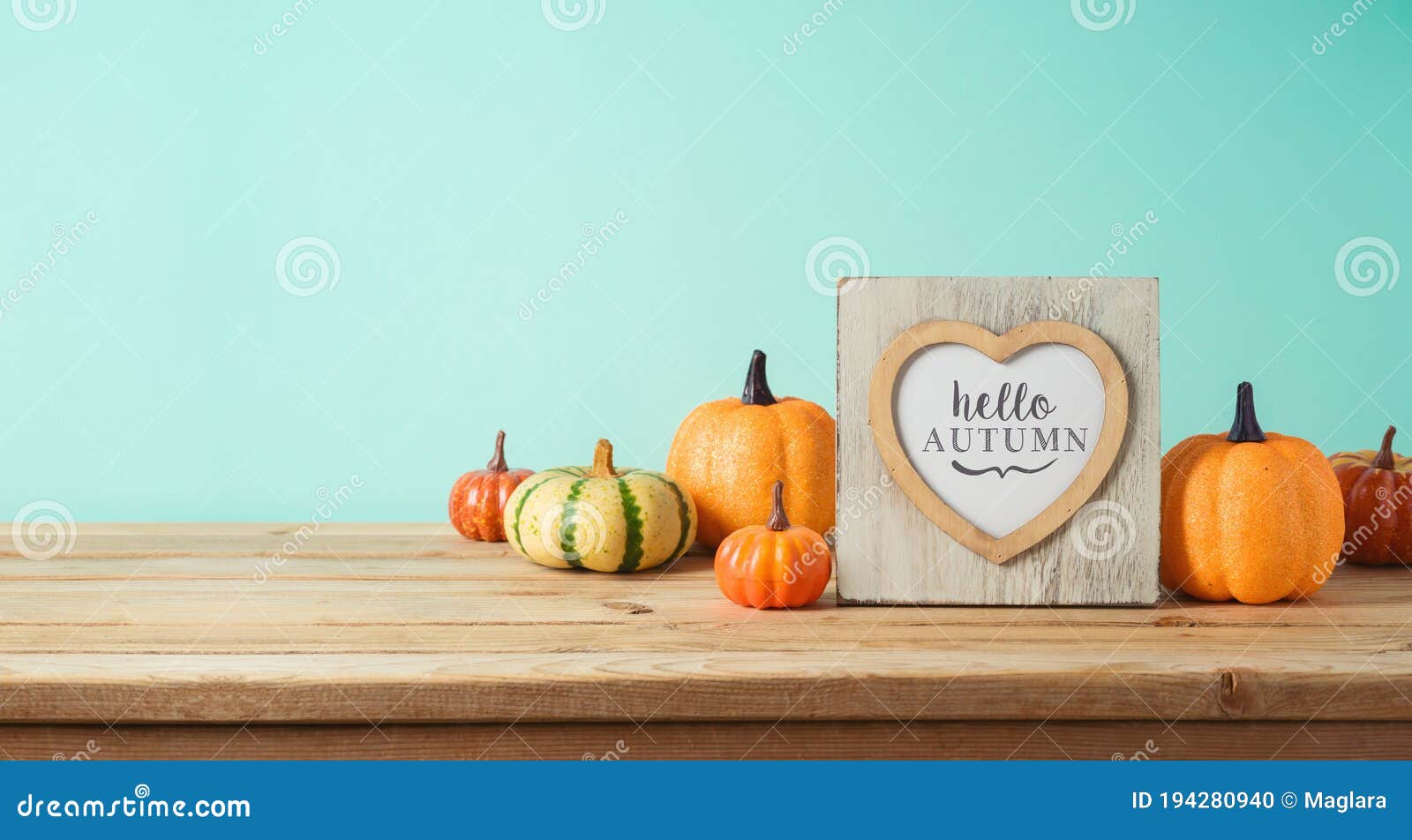 hello autumn concept with photo frame and pumpkin decor on wooden table over blue background. fall season greeting card
