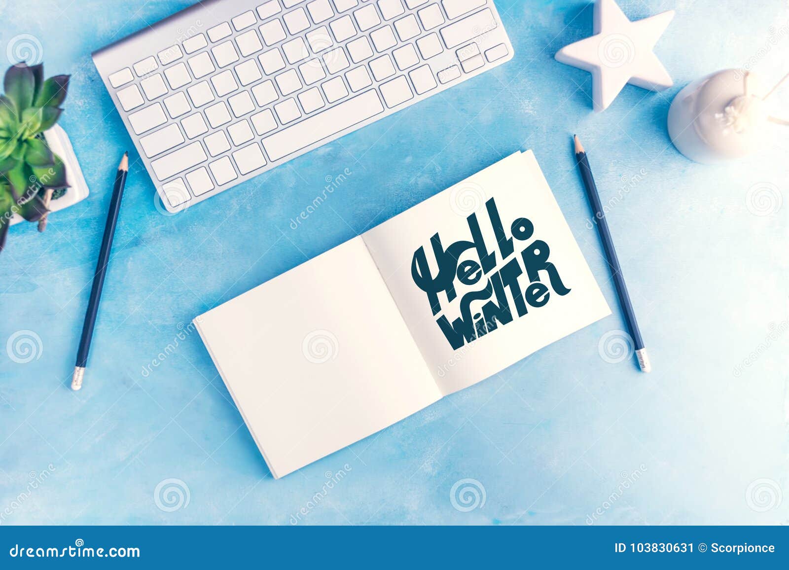 hello winter graphic handlettering in open notebook with keyboard on blue table top view flat lay mock up