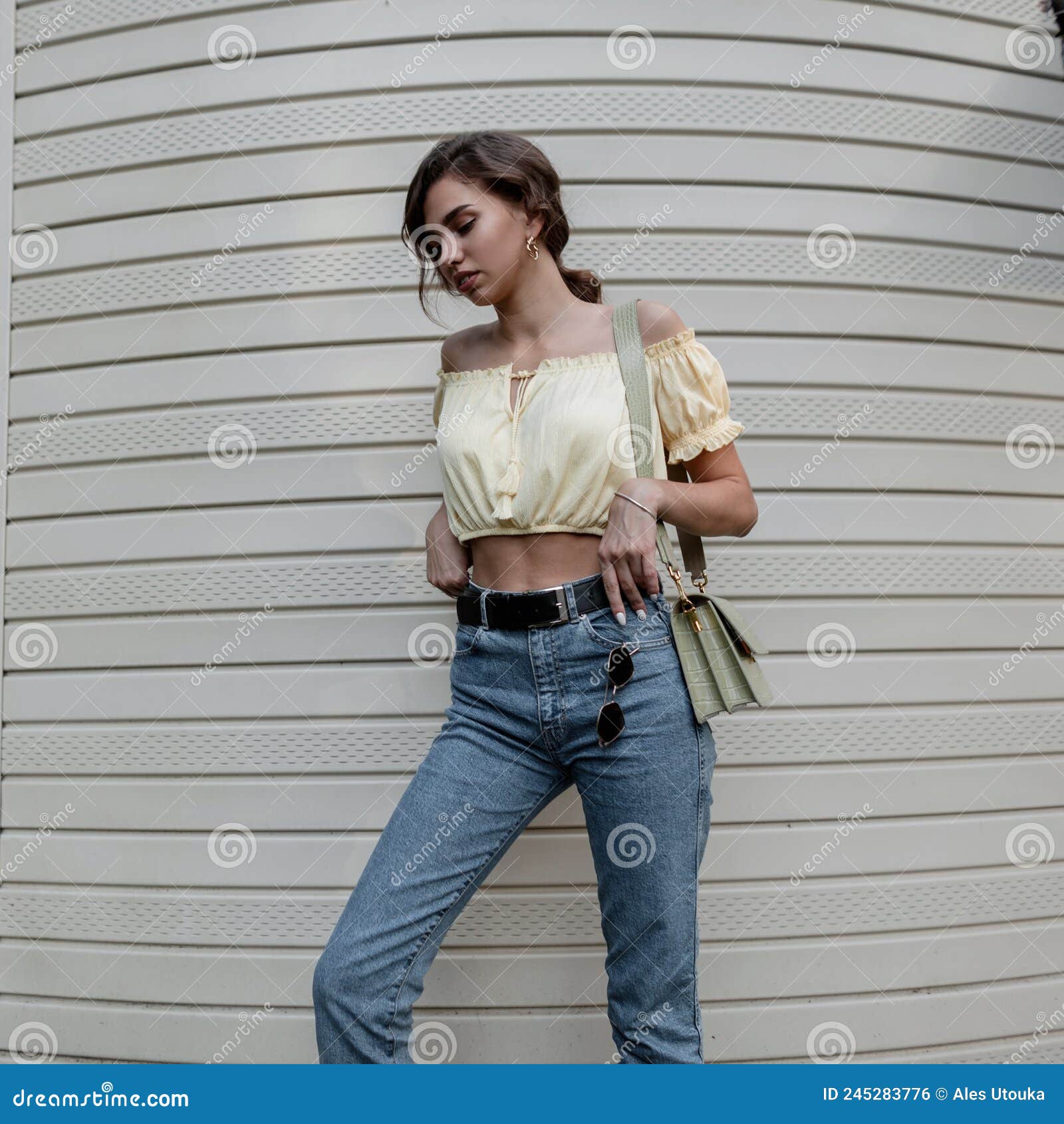 Hermosa Mujer Elegante Y Rizada En Una Moderna Blusa Amarilla En Jeans  Informales Azules Con Un Bolso De Mano Verde De Moda Foto de archivo -  Imagen de lifestyle, lindo: 245283776