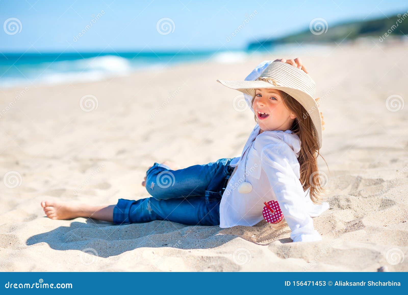 Una niña de sombrero azul de pie junto a la playa al atardecer