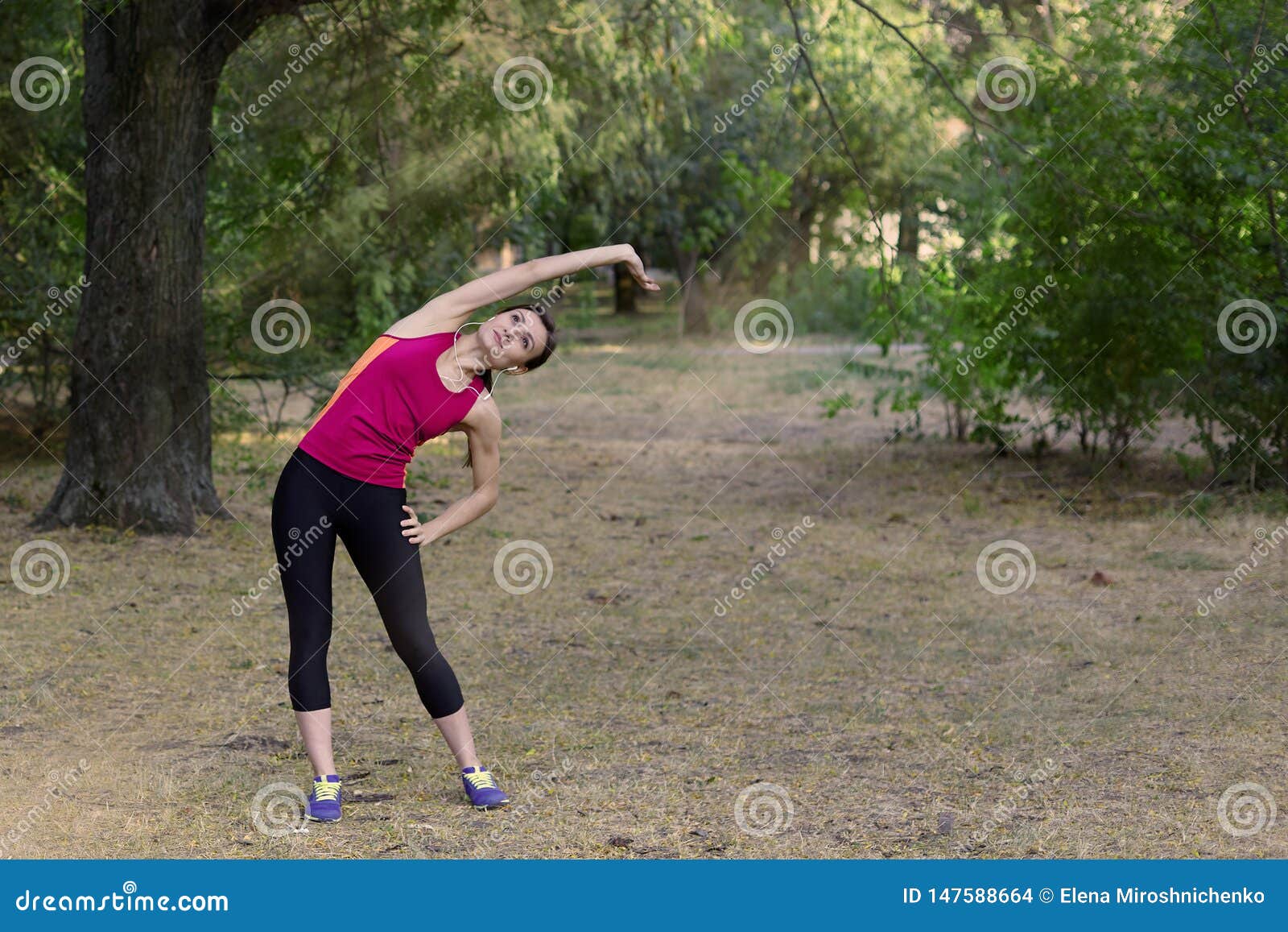 Herrliche junge dünne Frau macht Turnhalle im Morgenpark Seitenneigung, helle Sportkleidung, weiße Kopfhörer, Stille und Atmosphä. Herrliche junge dünne Frau macht Turnhalle im Morgenpark Seitenneigung, helle Sportkleidung, weiße Kopfhörer, Stille und die Atmosphäre, Training ausdehnend sich entspannen Drau?en Kopienraum