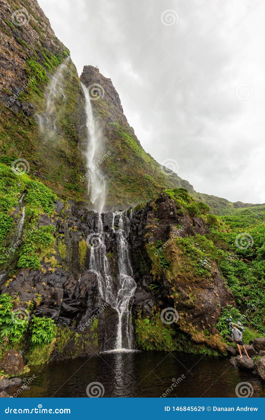 Het bezoeken van de Azoren. FAJA GRANDE, PORTUGAL - AUGUSTUS 7: Een niet geïdentificeerde toerist zit onder Cascata do Poco doet Bacalhau-waterval in Faja Grande op 7 Augustus, 2017