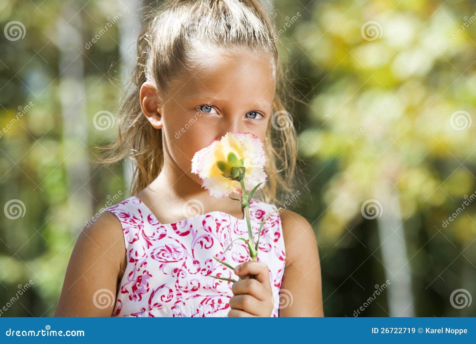 Het blauwe eyed meisje verbergen achter bloem. Sluit omhoog portret van het blauwe eyed meisje verbergen achter bloem in openlucht.