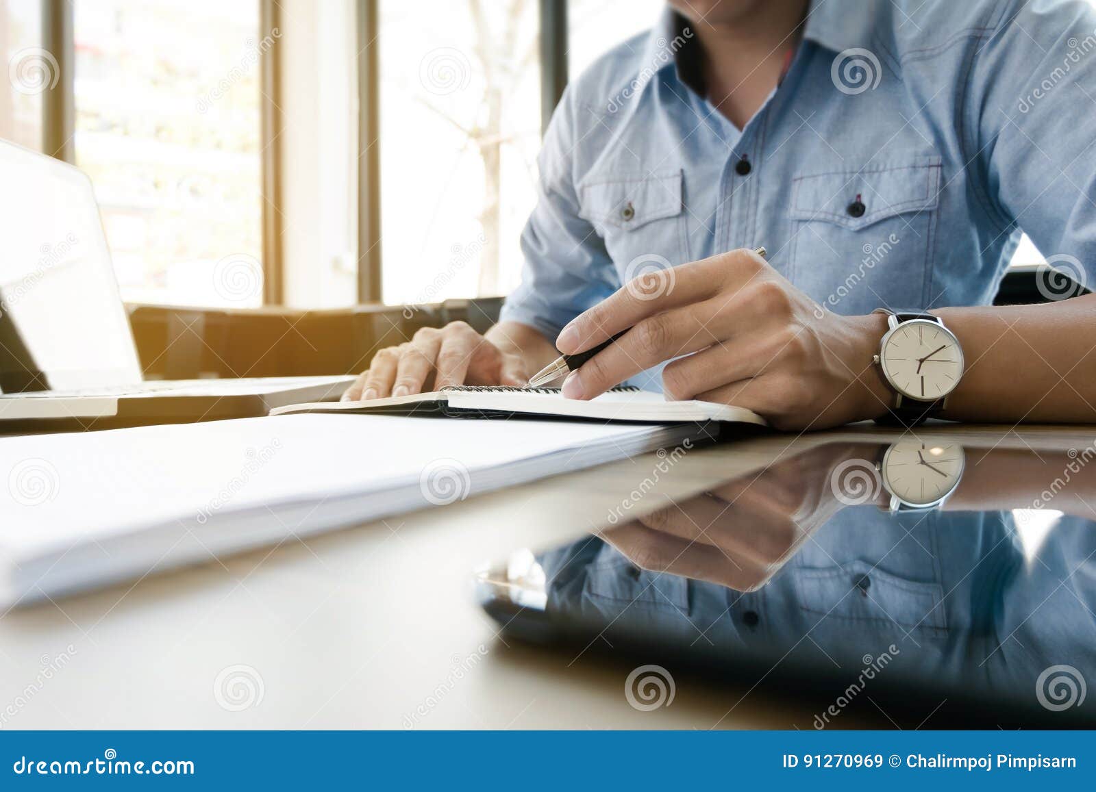 Het jonge directeurwerk in modern bureau op notitieboekje en computerlaptop