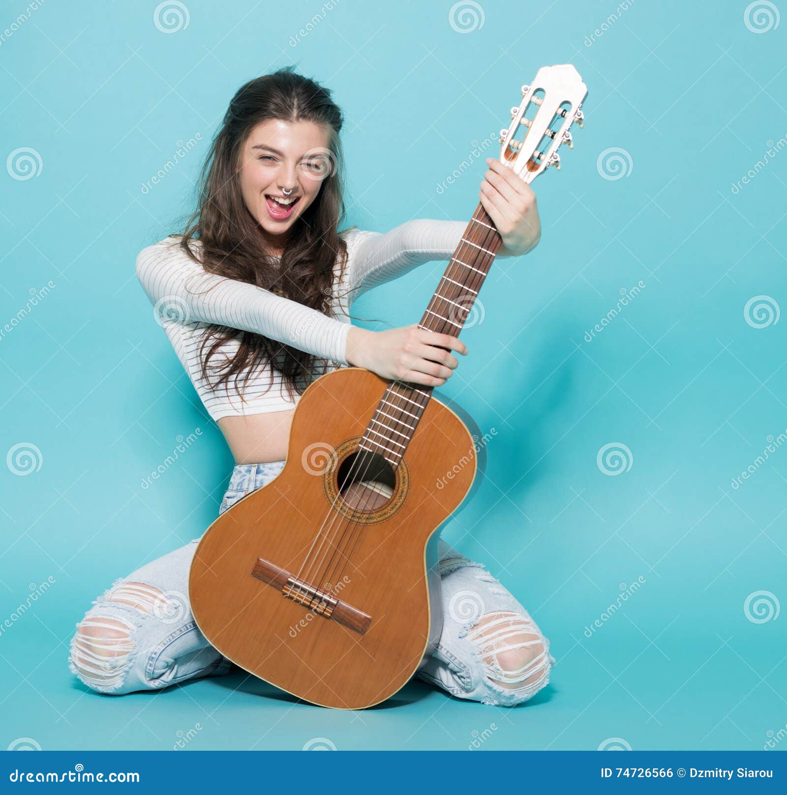Het glimlachen het mooie jonge meisje stellen met gitaar