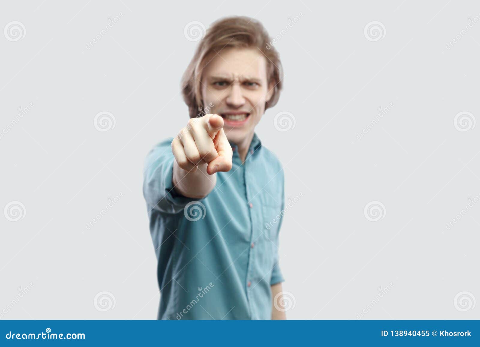 hey you. portrait of serious blame handsome long haired blonde young man in blue casual shirt standing, pointing, alarming and