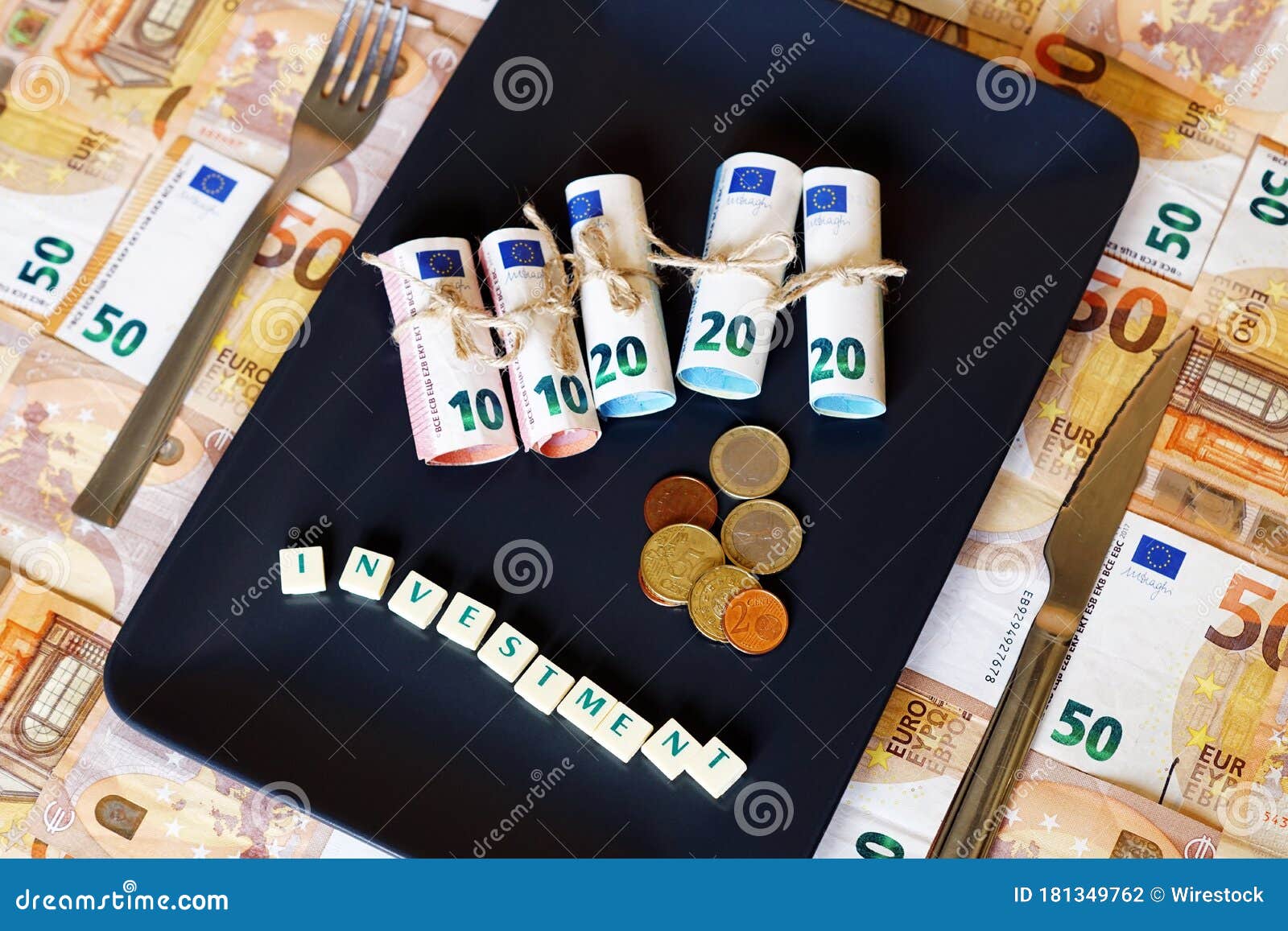 high angle shot of dinero money bills in a plate with a fork and white cubes spelling investment