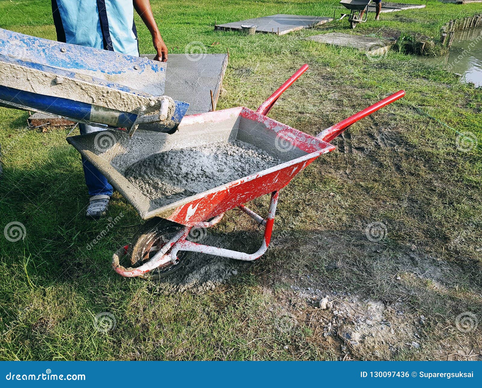 Worker Pouring Mixed Cement into Red Wheelbarrow at Construction Site