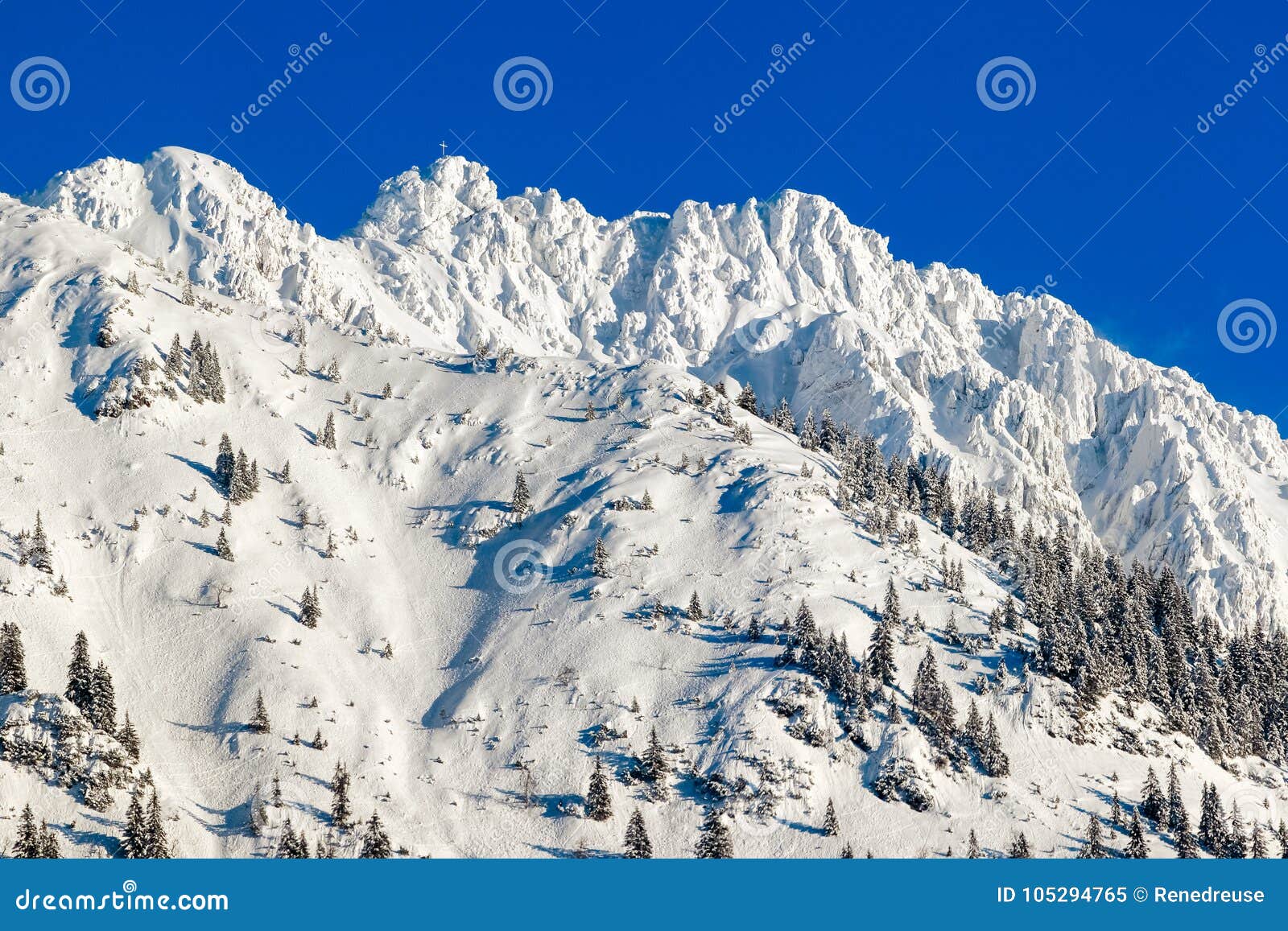 high mountain with summit cross under deep snow in winter. rauhhorn, allgau, bavaria in germany.