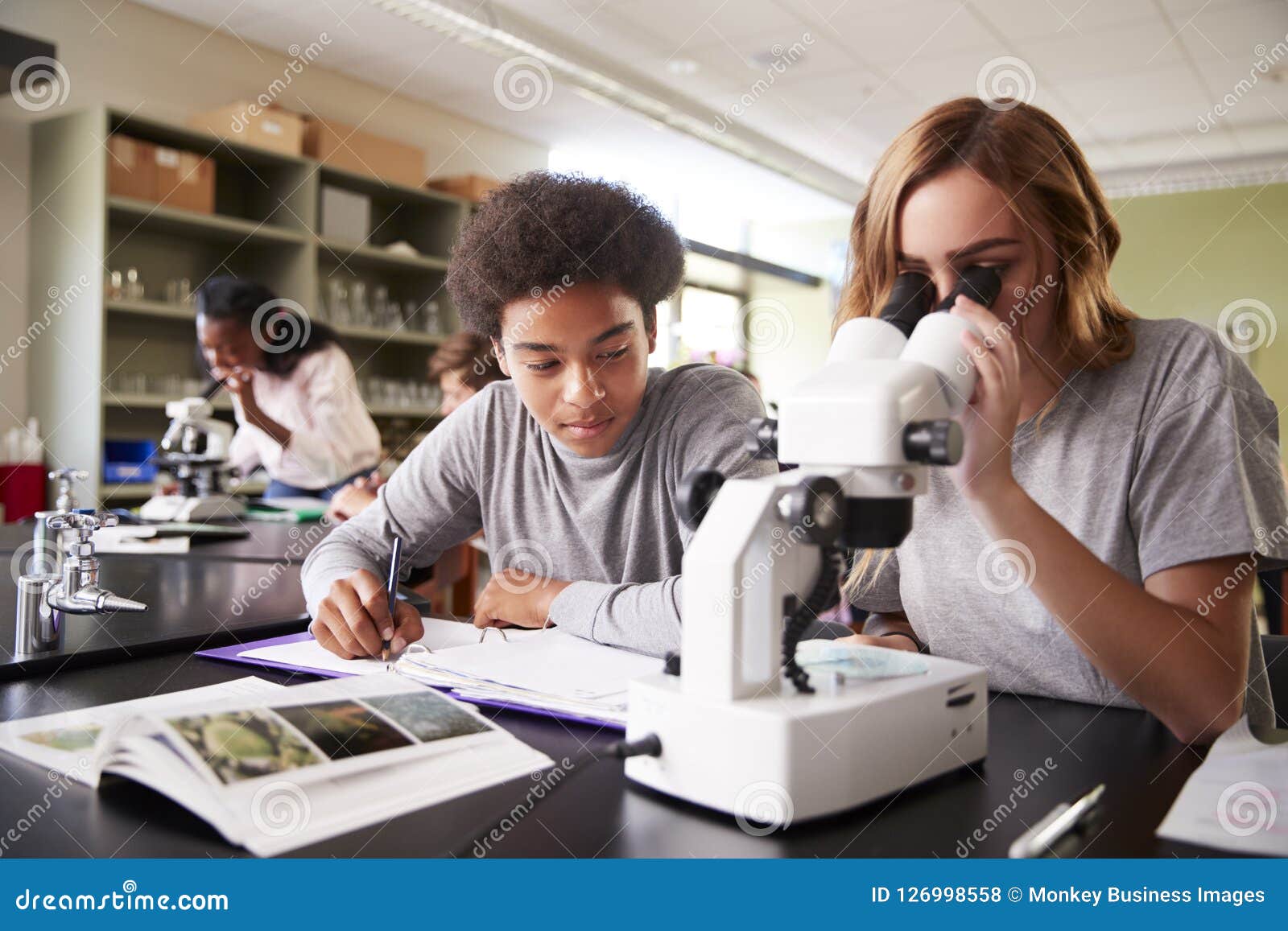 high school students looking through microscope in biology class