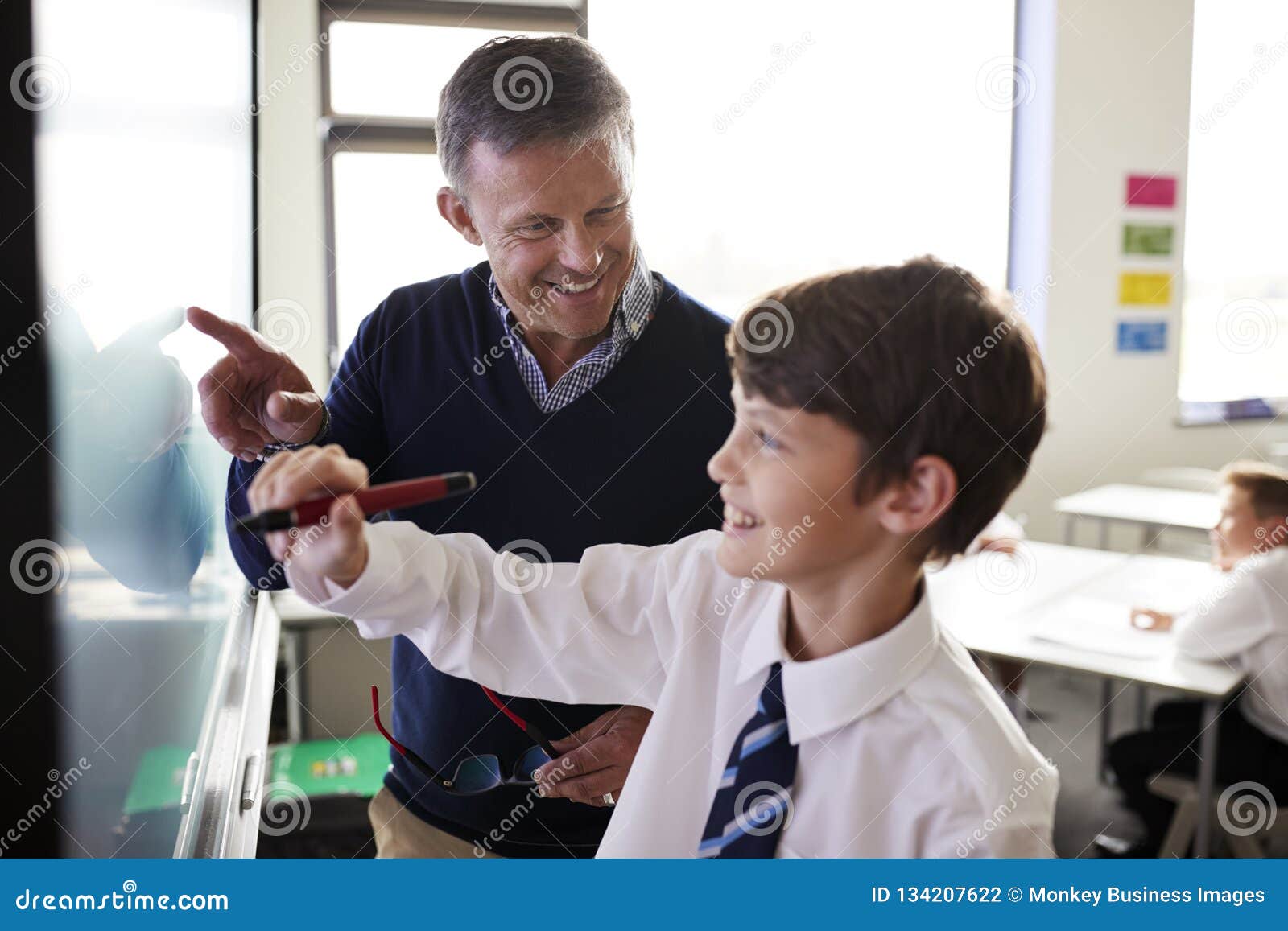high school teacher with male student wearing uniform using interactive whiteboard during lesson