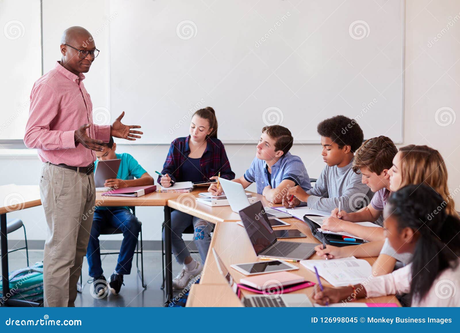 high school teacher talking to pupils using digital devices in technology class