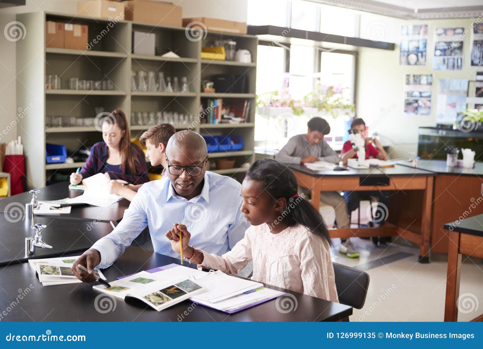 high school tutor sitting at desk with female student in biology class