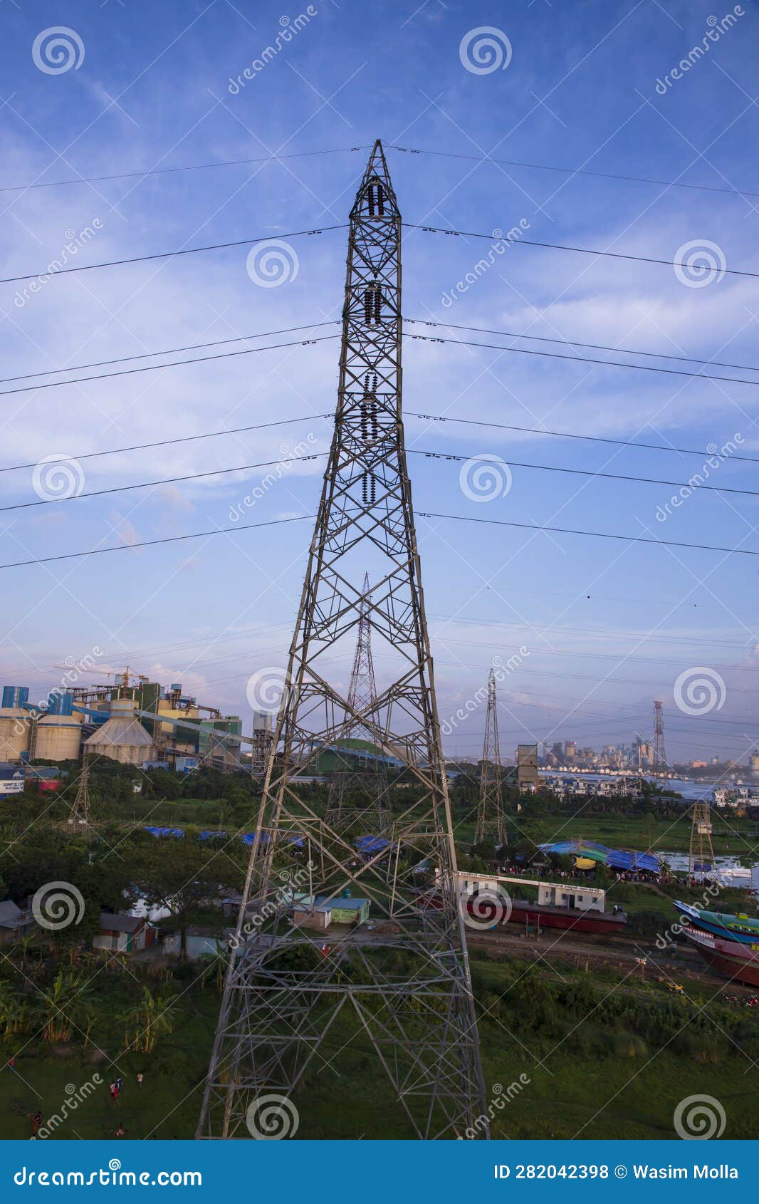 High Voltage Electricity Pylon with Cityscape and Blue Sky Background