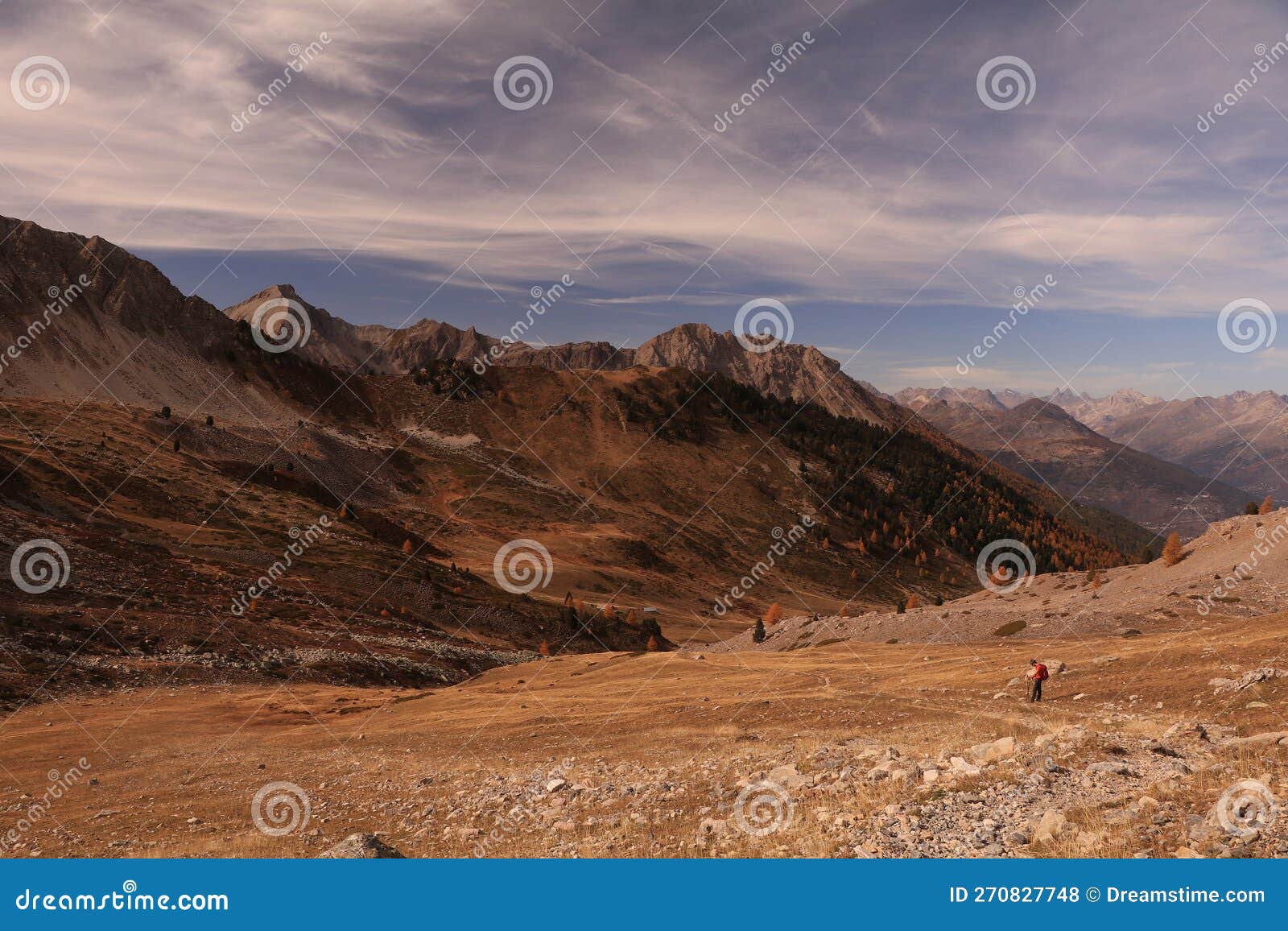 a hiker going down towards a valley in the rocky mountains in the autumn with clouy sky