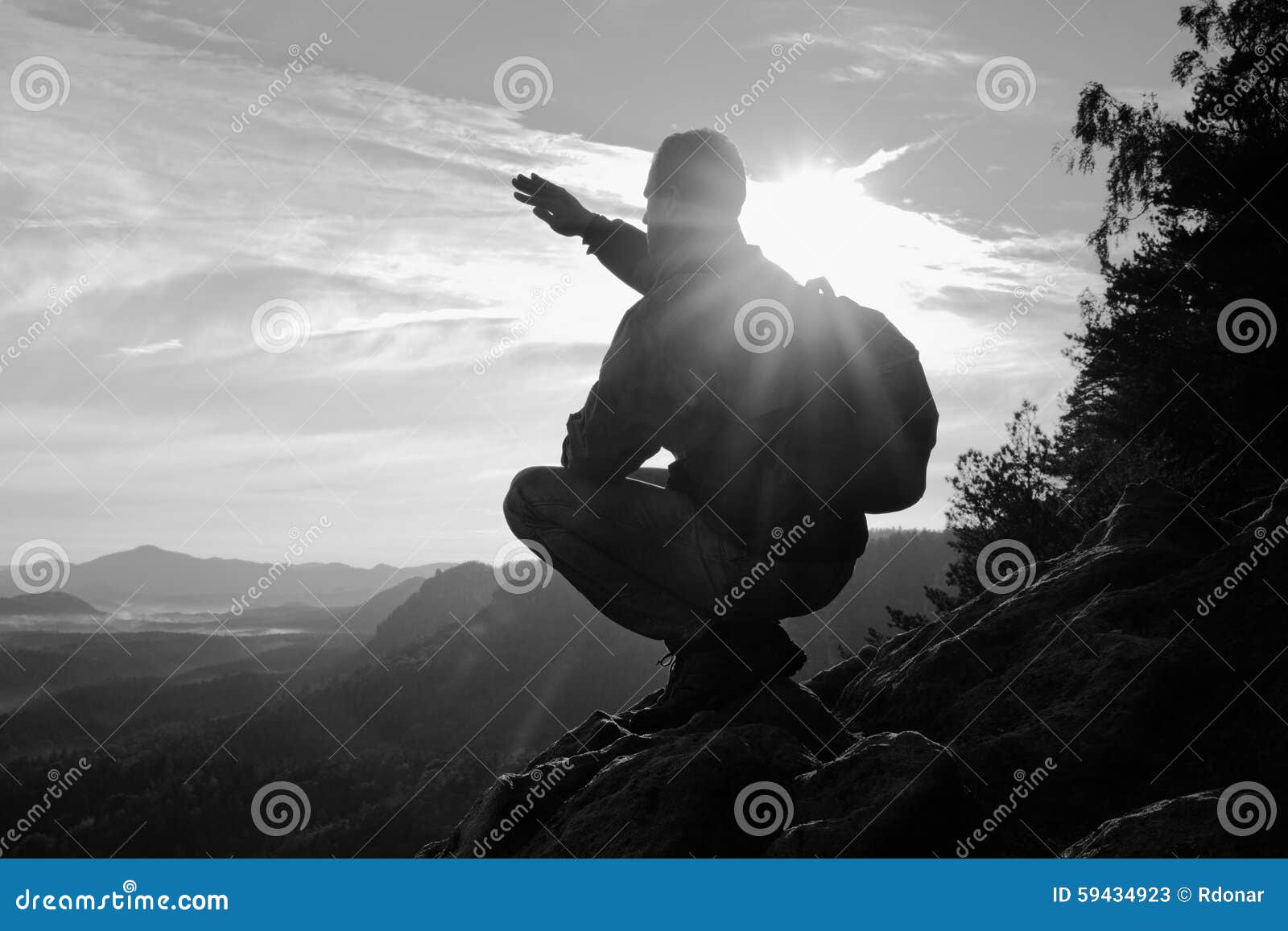 Hiker With Sporty Backpack Sit On Rocky Cliff Edge And Watching Into Misty Valley Bellow Sunny 