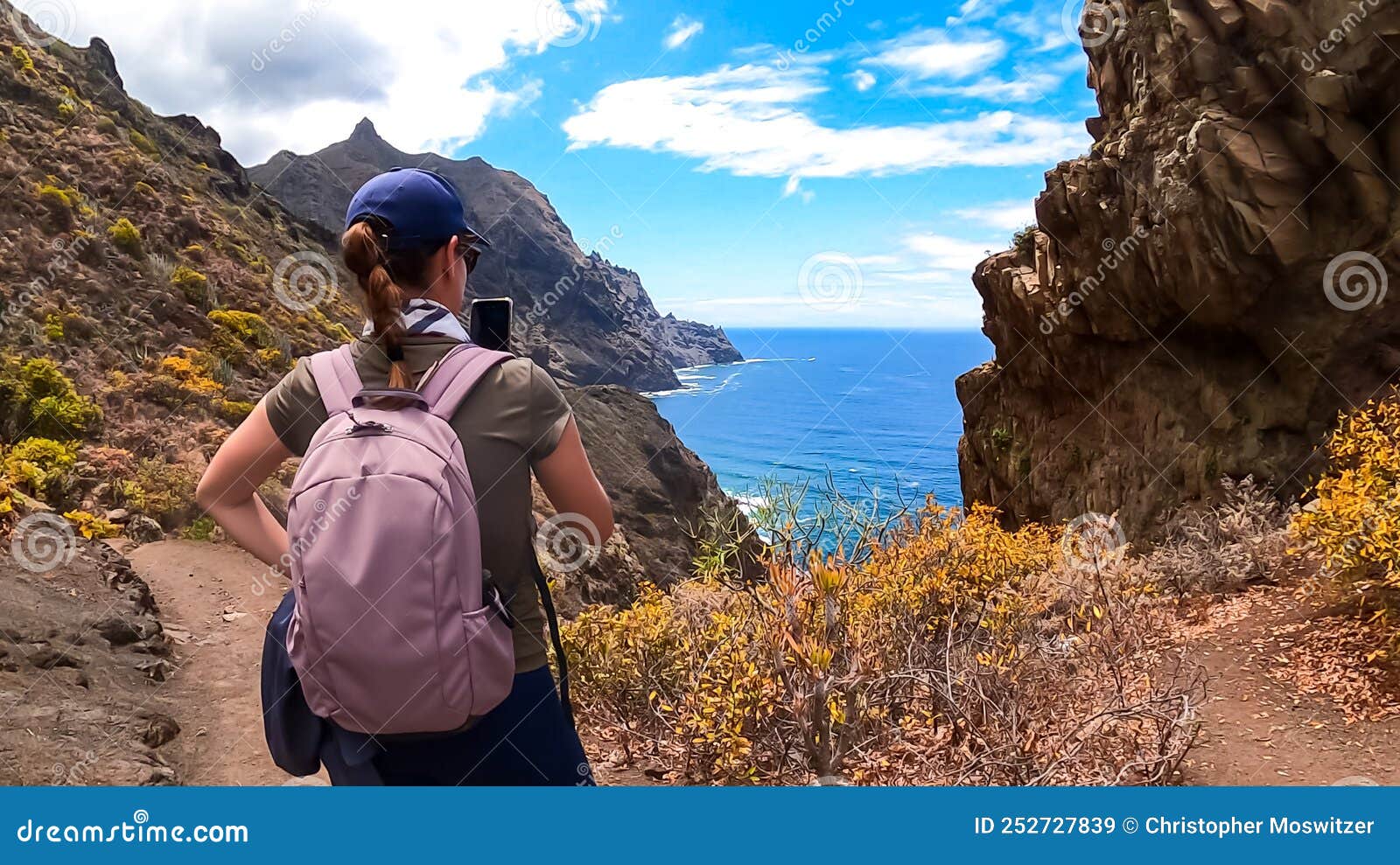 hiking woman taking picture of scenic view of coastline of anaga mountain range on tenerife, canary islands, spain, europe