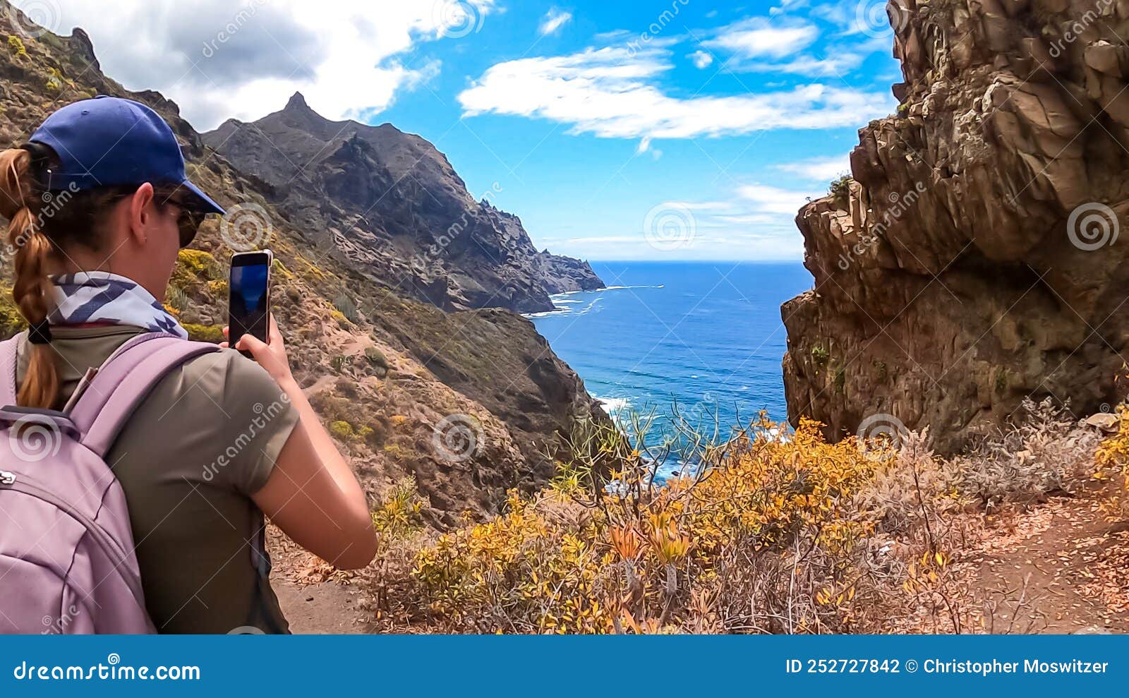hiking woman taking picture of scenic view of coastline of anaga mountain range on tenerife, canary islands, spain, europe