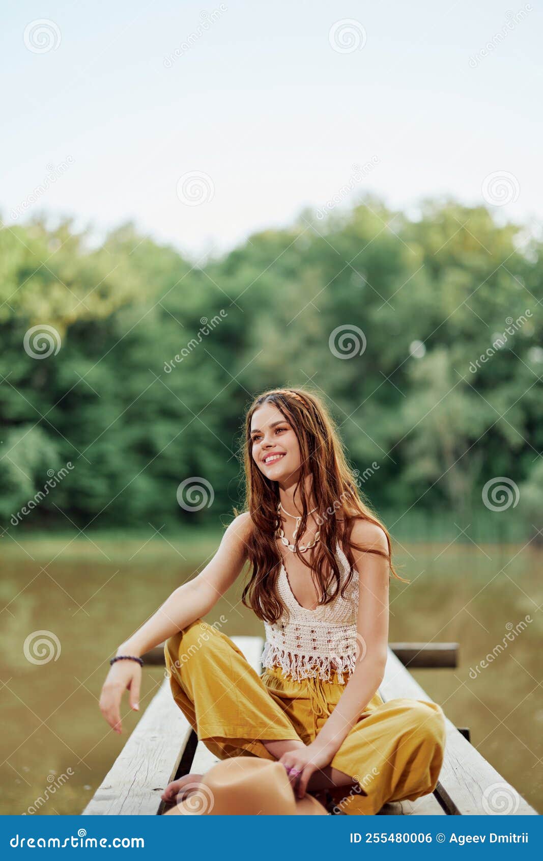 A Hippie Woman Sits on a Bridge by a Lake on a Nature Trip and Smiles ...
