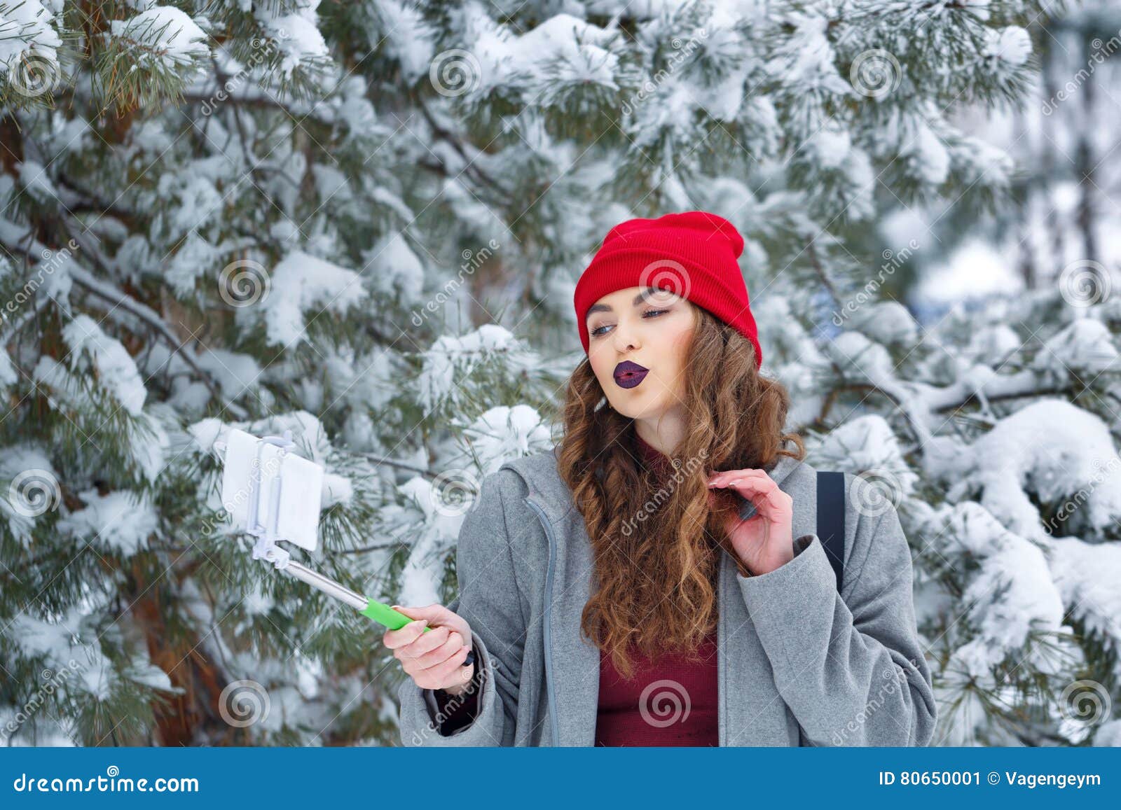 A woman in winter clothes walks in the park. Takes a selfie. There