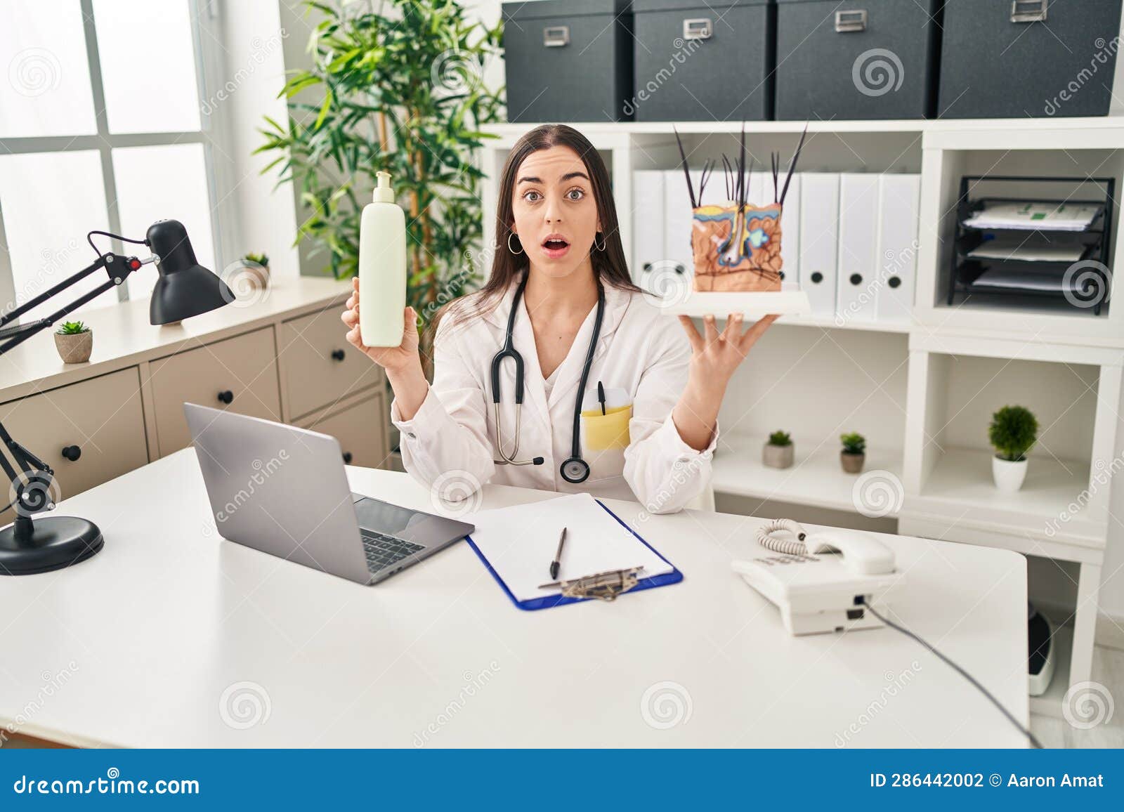 hispanic doctor woman holding model of human anatomical skin and hair afraid and shocked with surprise and amazed expression, fear