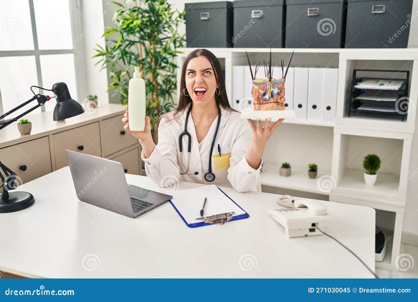 hispanic doctor woman holding model of human anatomical skin and hair angry and mad screaming frustrated and furious, shouting