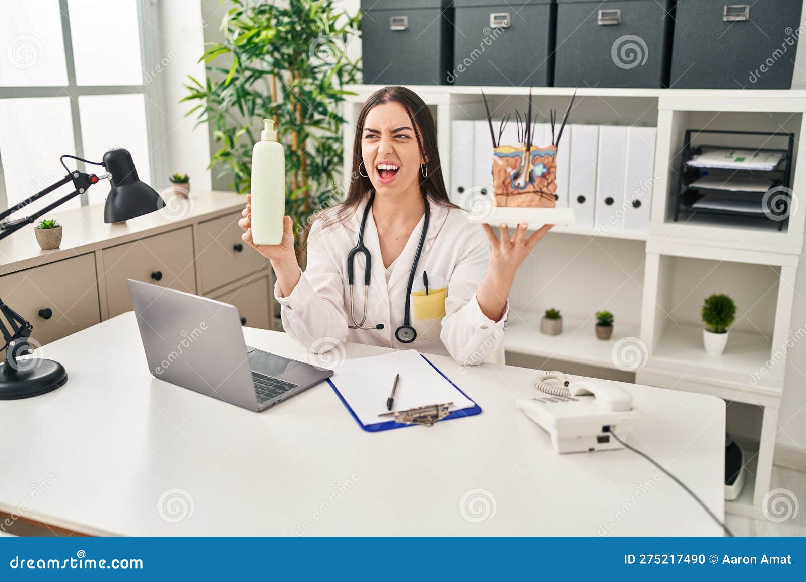 hispanic doctor woman holding model of human anatomical skin and hair angry and mad screaming frustrated and furious, shouting