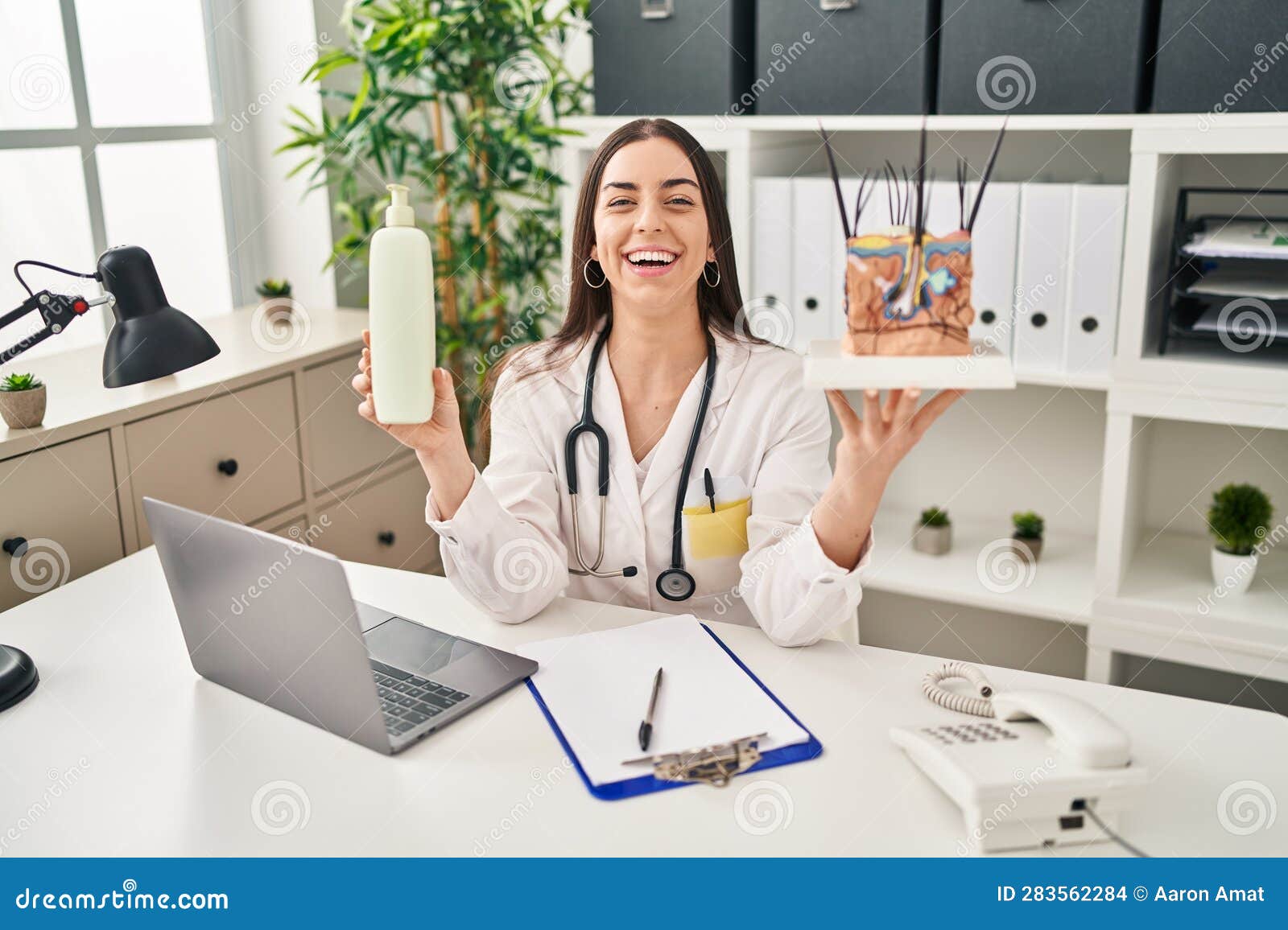 hispanic doctor woman holding model of human anatomical skin and hair smiling and laughing hard out loud because funny crazy joke